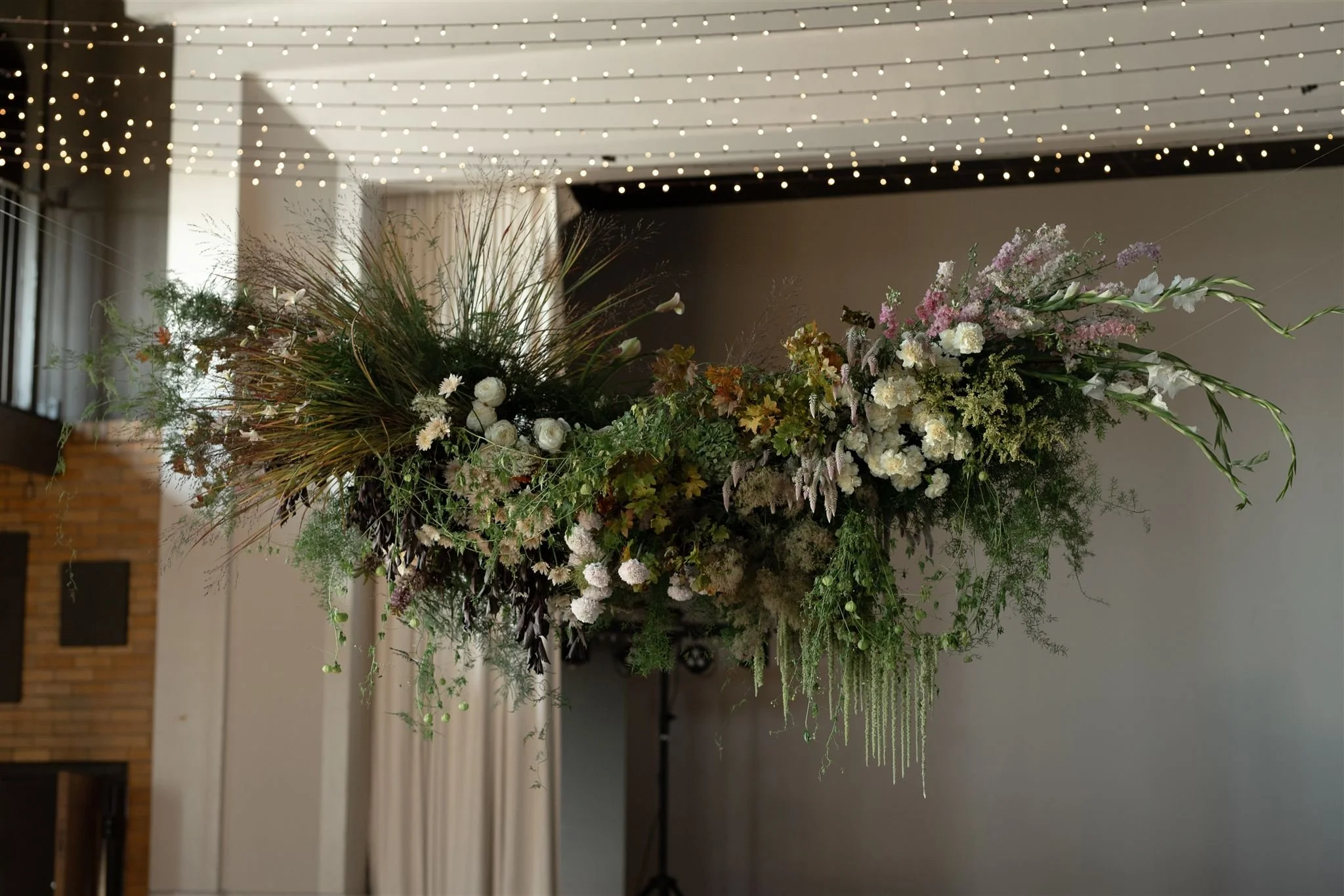 A large suspended floral arrangement with white and pink flowers and greenery in an indoor event space.