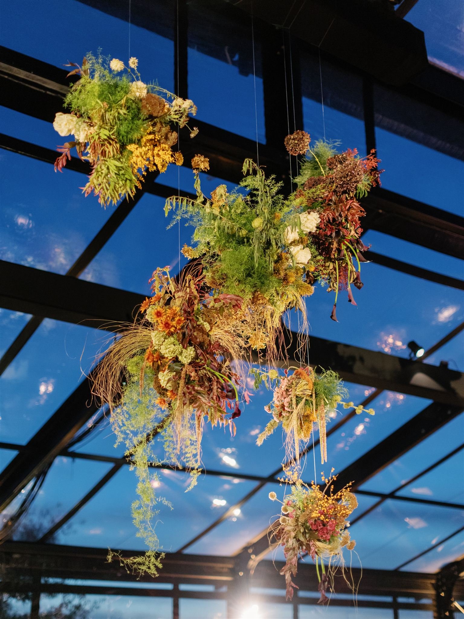 A hanging arrangement of dried flowers and foliage against a sky-blue background with glass panels.