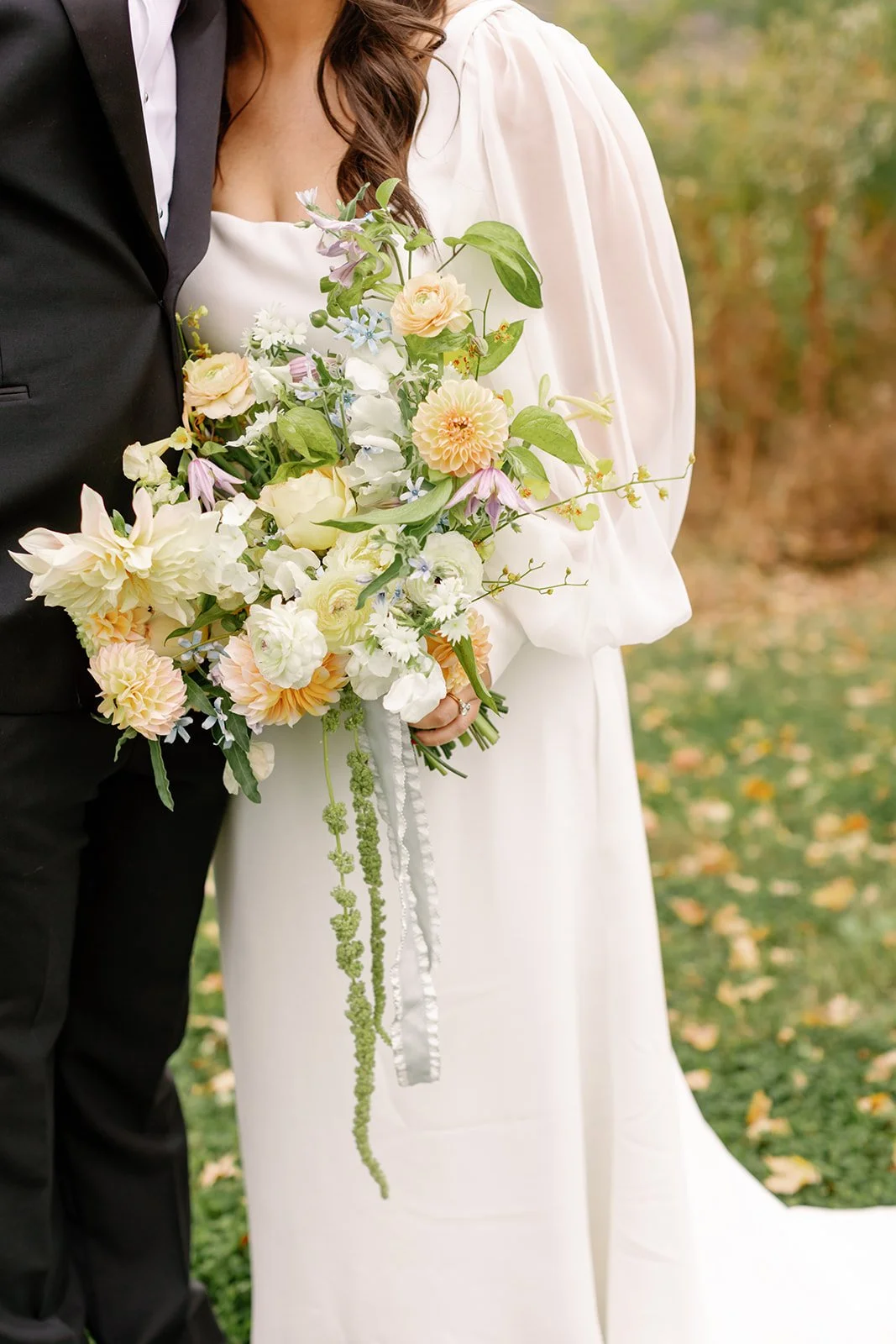 Close-up of a bride and groom standing outdoors, with the bride holding a large bouquet of pastel-colored flowers.