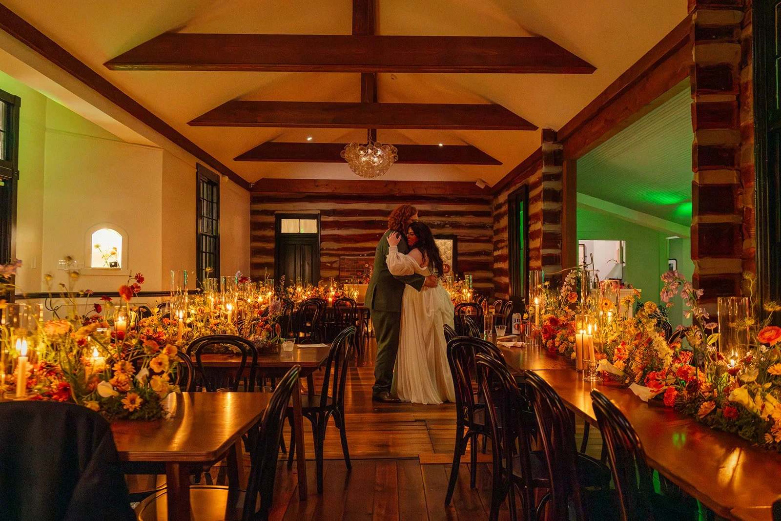 A bride and groom dance in a warmly-lit reception hall decorated with flowers and candles.