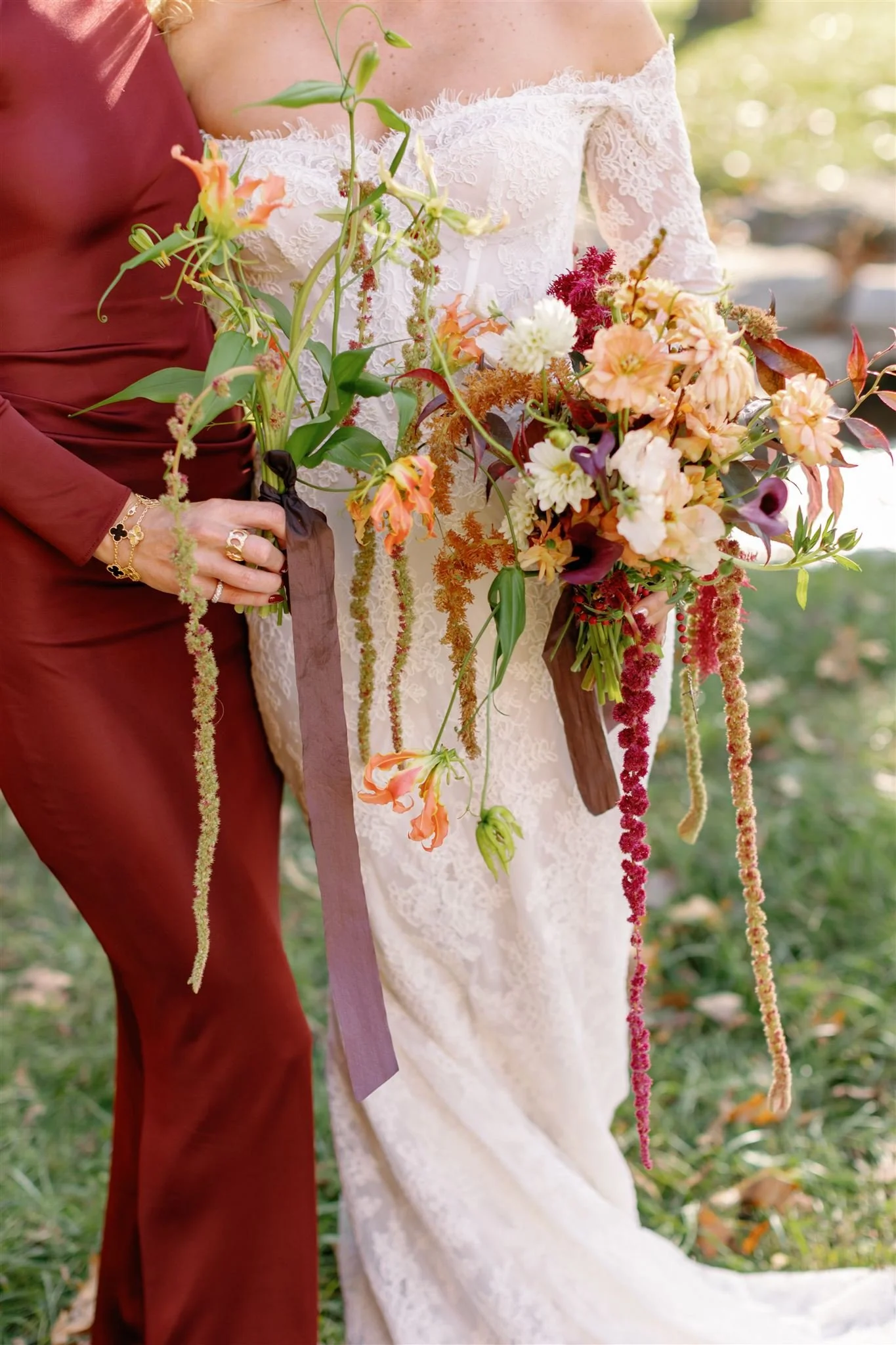 Close-up of a bride holding a colorful bouquet of flowers, standing next to another person in a maroon dress outdoors.