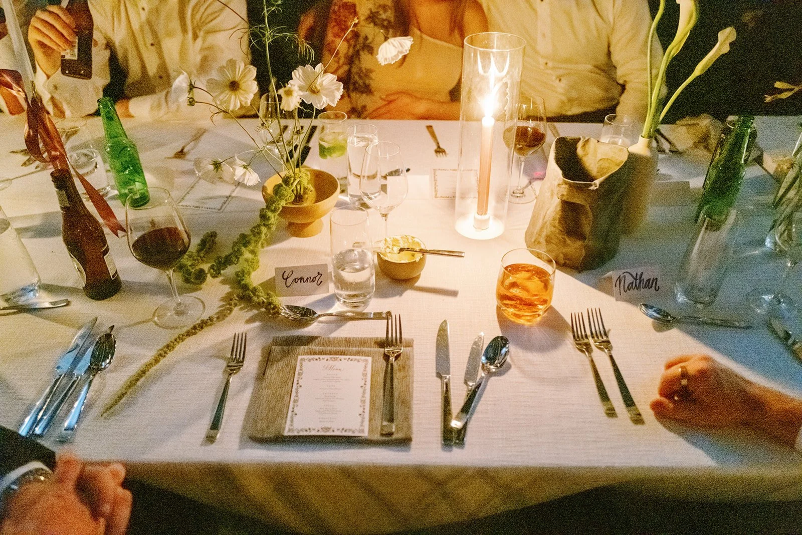 A dinner table setting with candles, flowers, drinks, and tableware, labeled with name cards 'Connor' and 'Nathan', at a formal event or celebration.