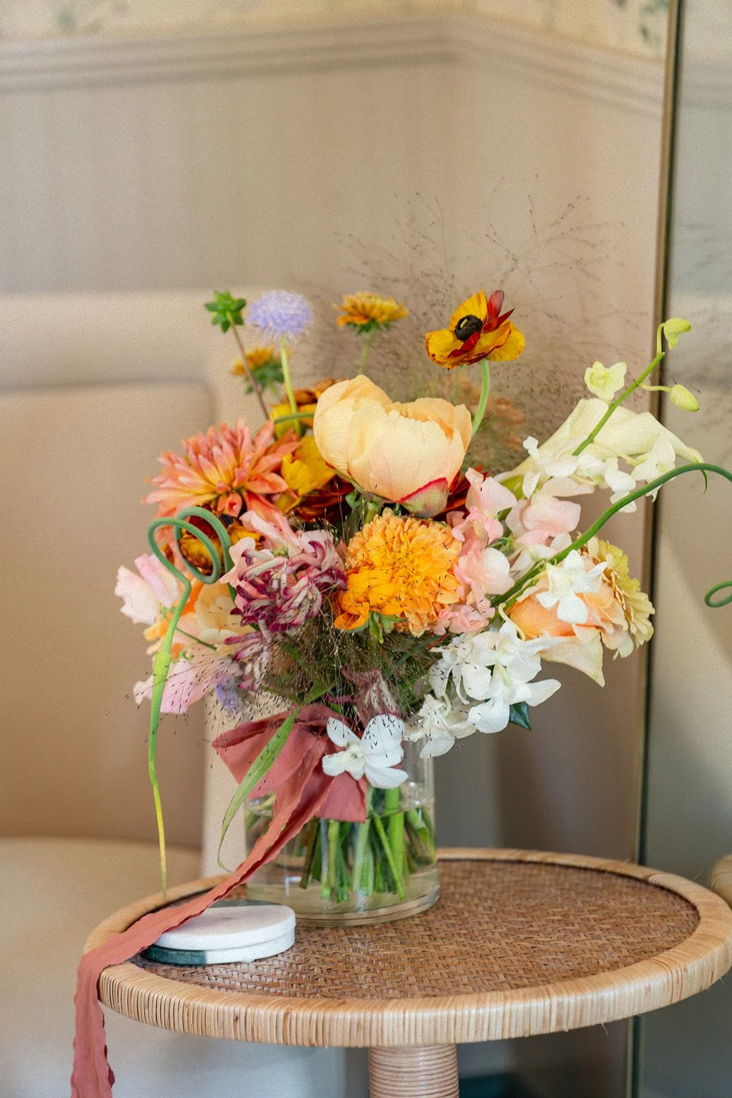 A colorful bouquet of mixed flowers in a glass vase placed on a round wooden table.