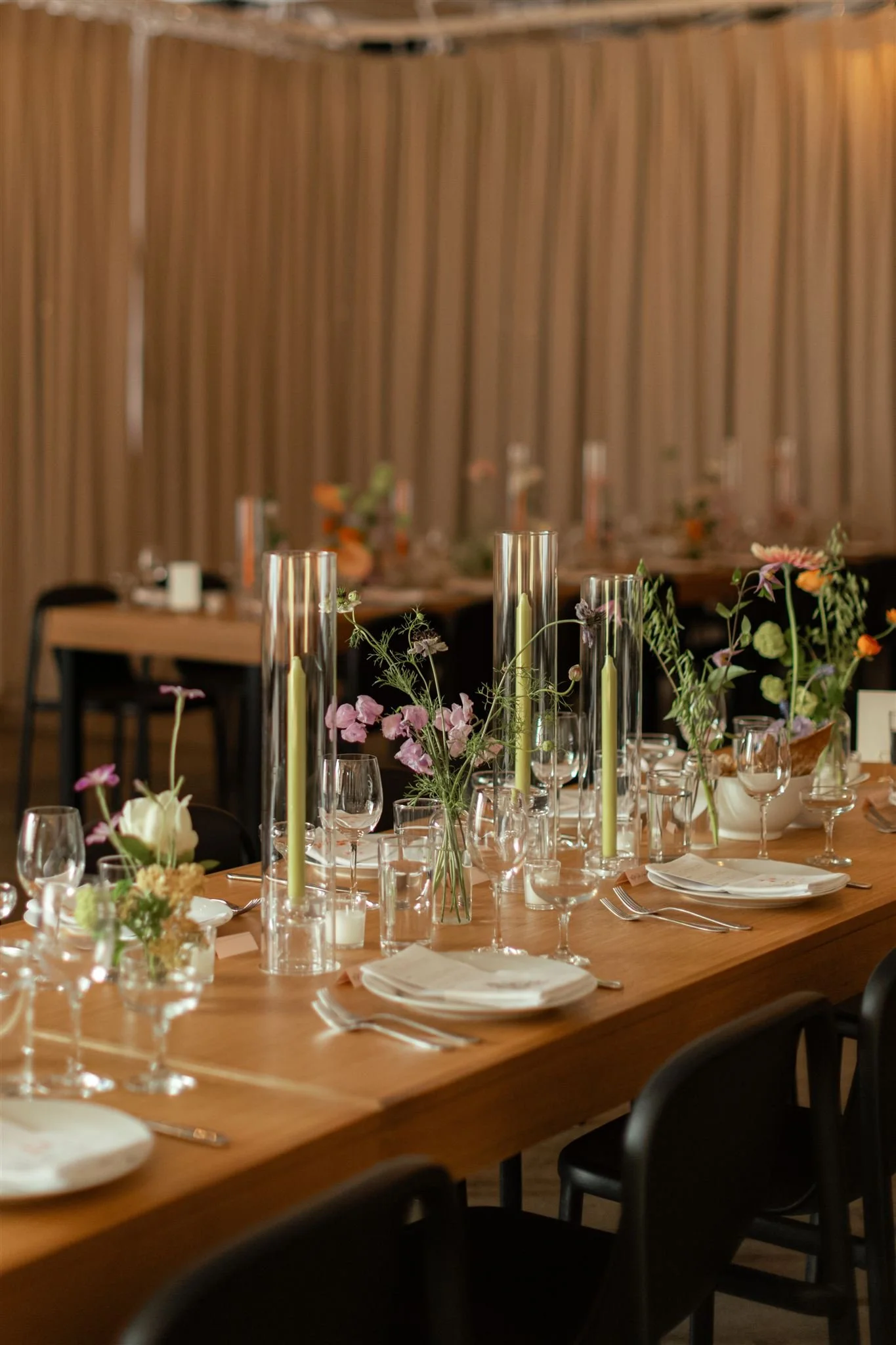 Decorated banquet table with floral centerpieces, candles, wine glasses, and plates, set for a formal event in an elegant venue.
