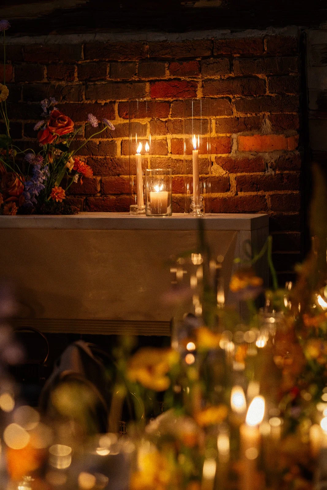 Candles and flowers on a table against a brick wall at night.