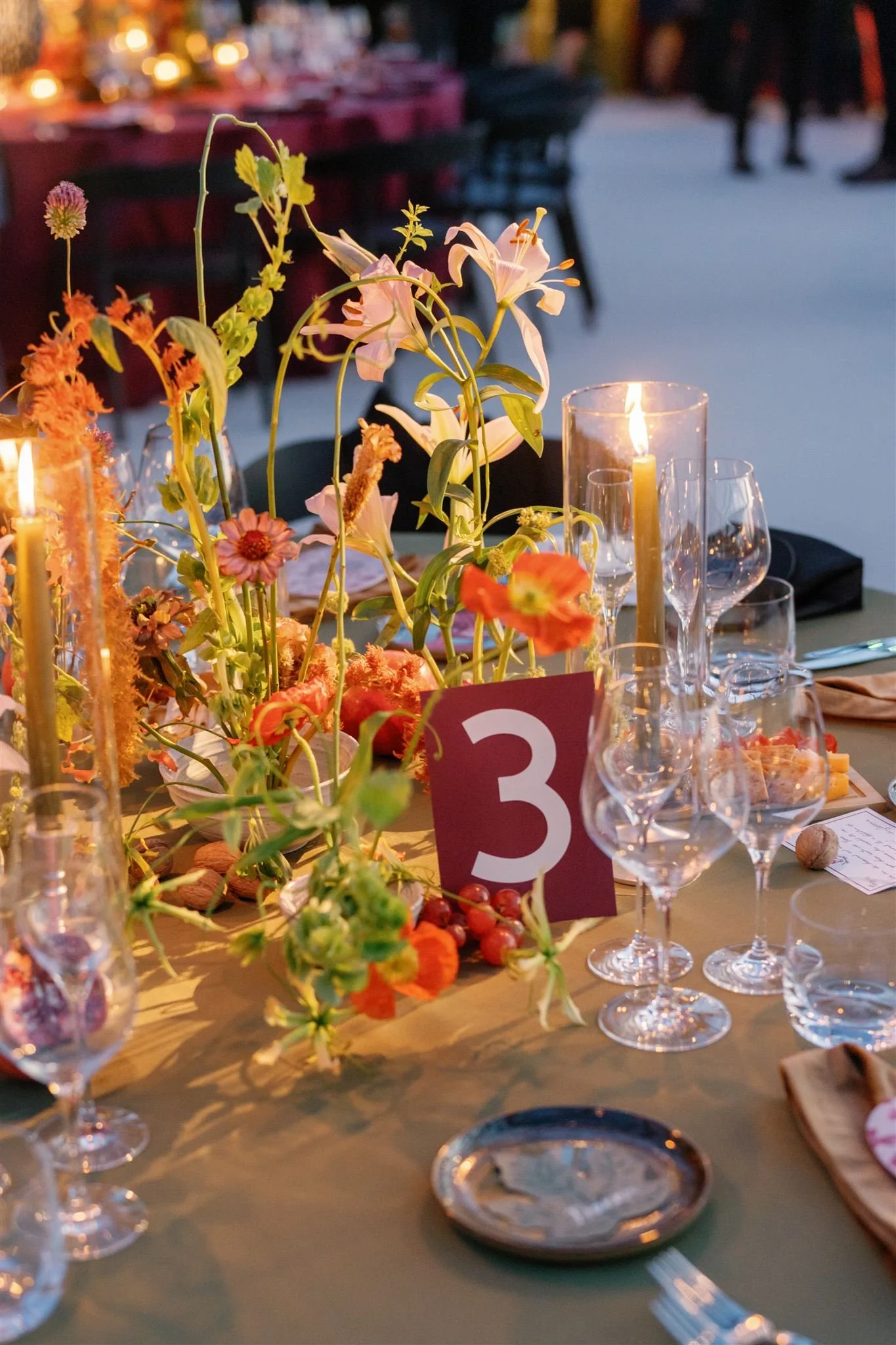 A dinner table decorated with flowers, candles, and glassware, with a table number 3 in the center, set for an event or celebration.