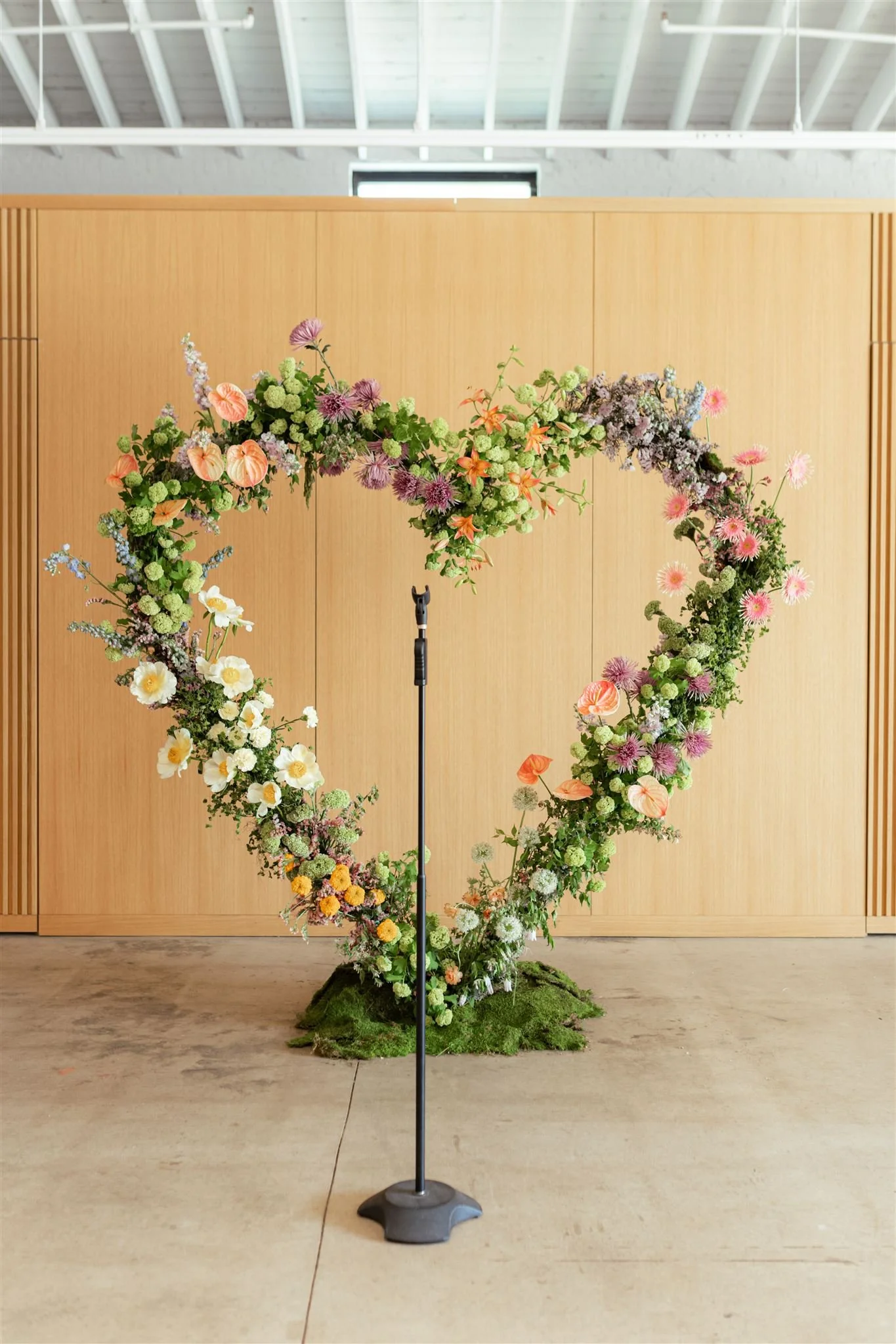 A heart-shaped floral arrangement on a stand in front of a wooden backdrop.