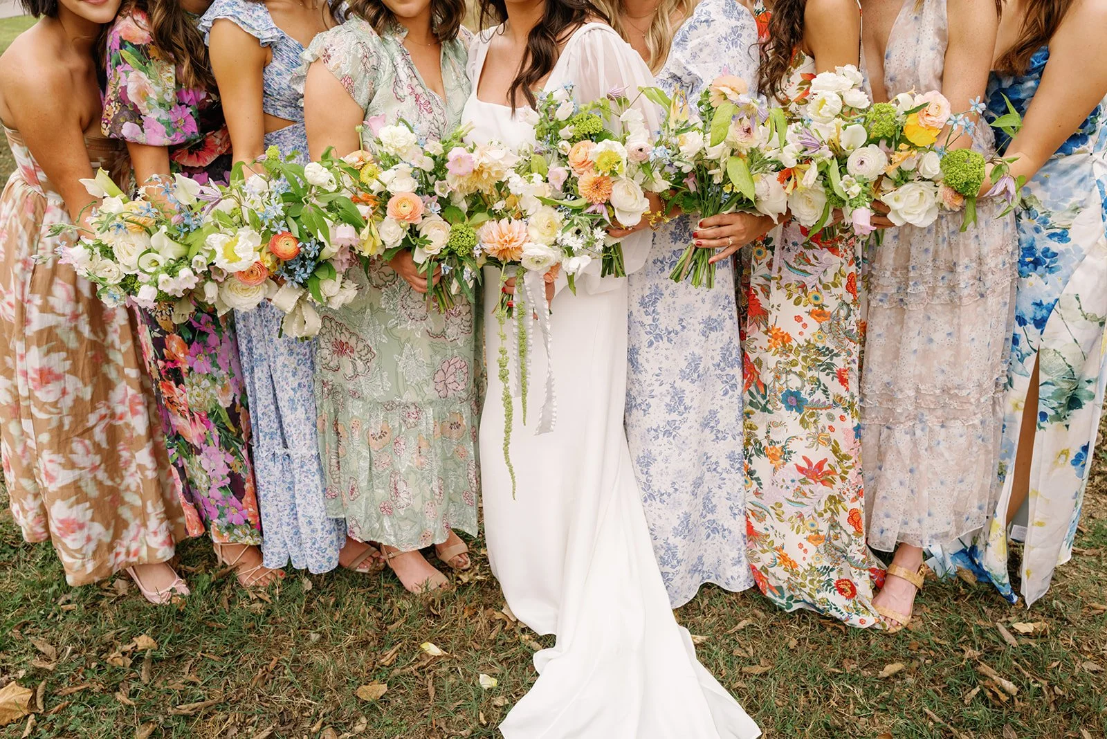 A line of women in colorful dresses holding bouquets of flowers at a wedding.