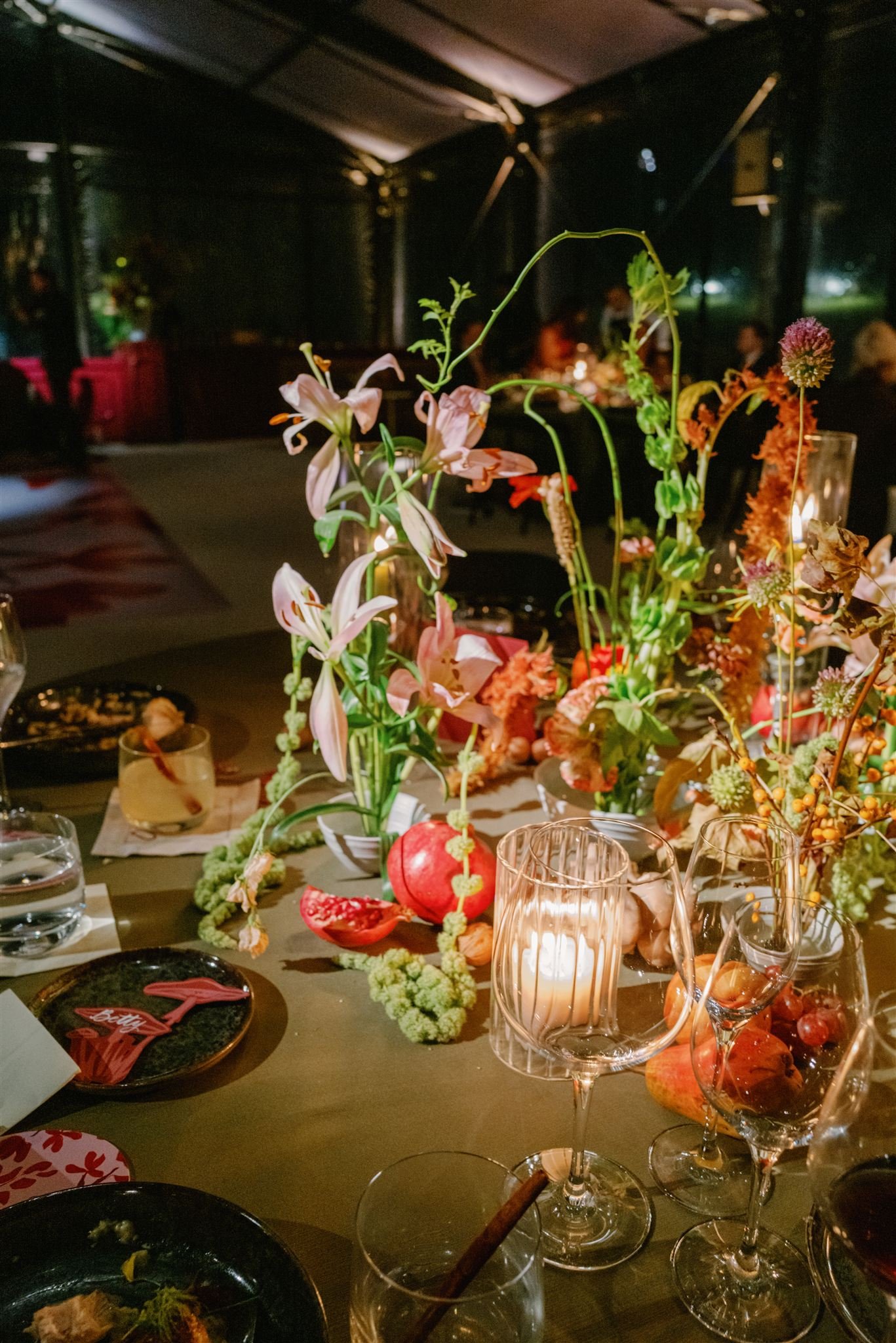 Decorated dinner table with floral centerpieces, candles, wine glasses, and plates, in a dimly lit event space.