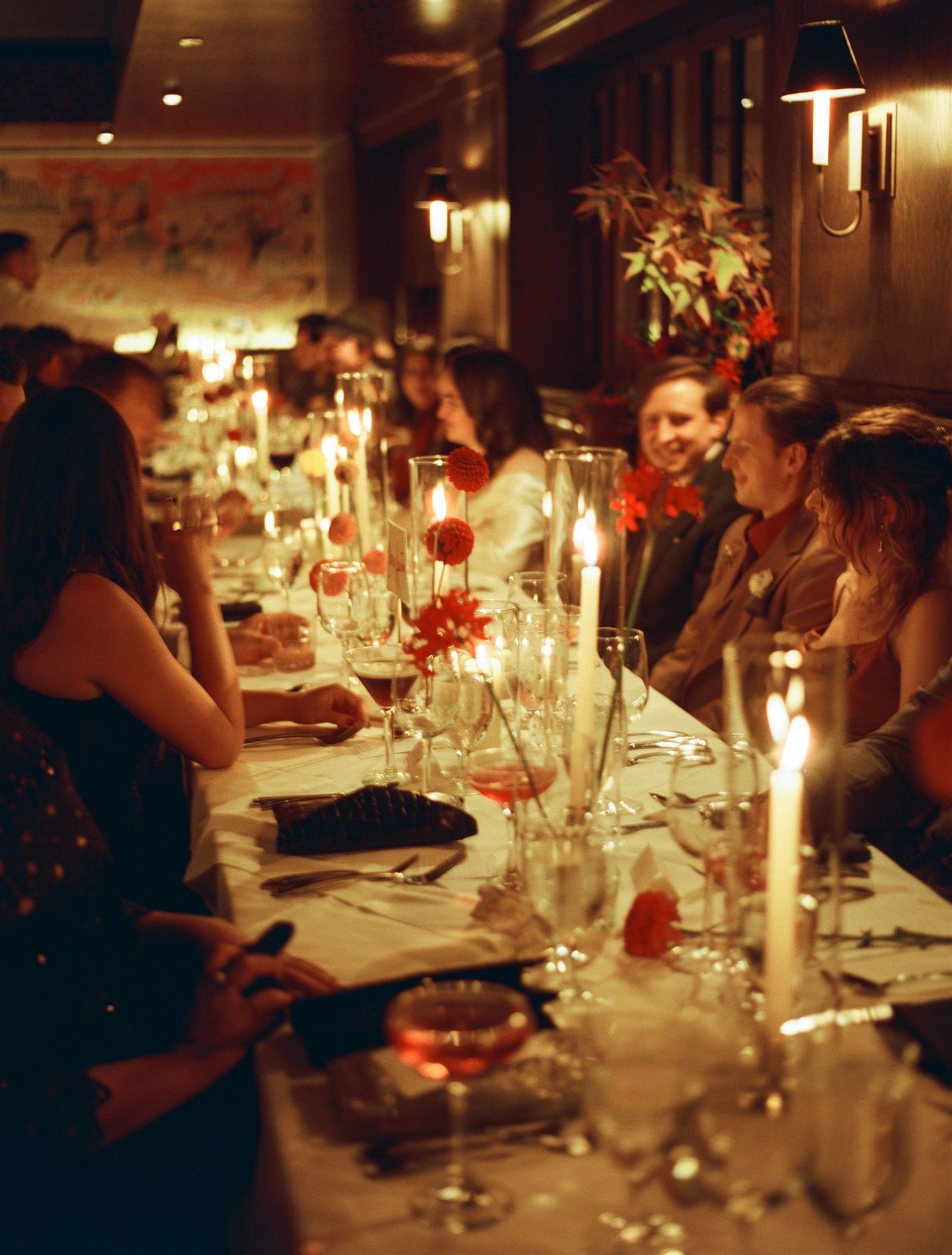 People dining at a long table decorated with candles and flowers in a dimly lit restaurant.