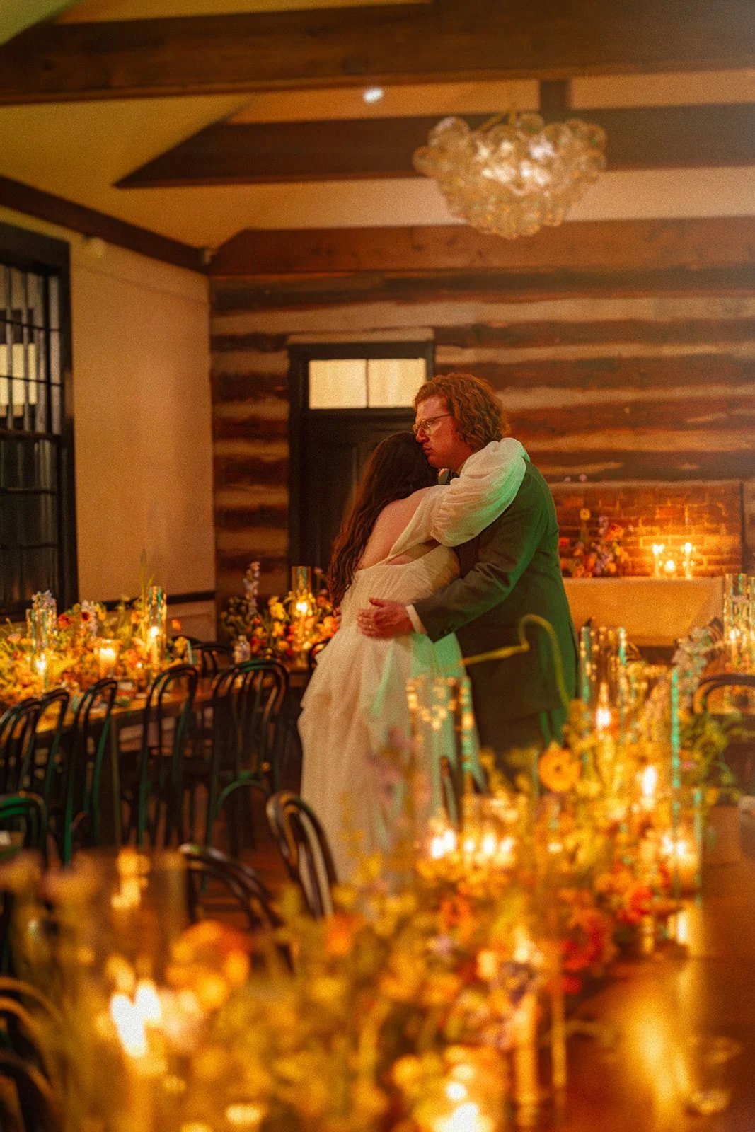A couple embracing on a decorated reception hall with candles and flowers.