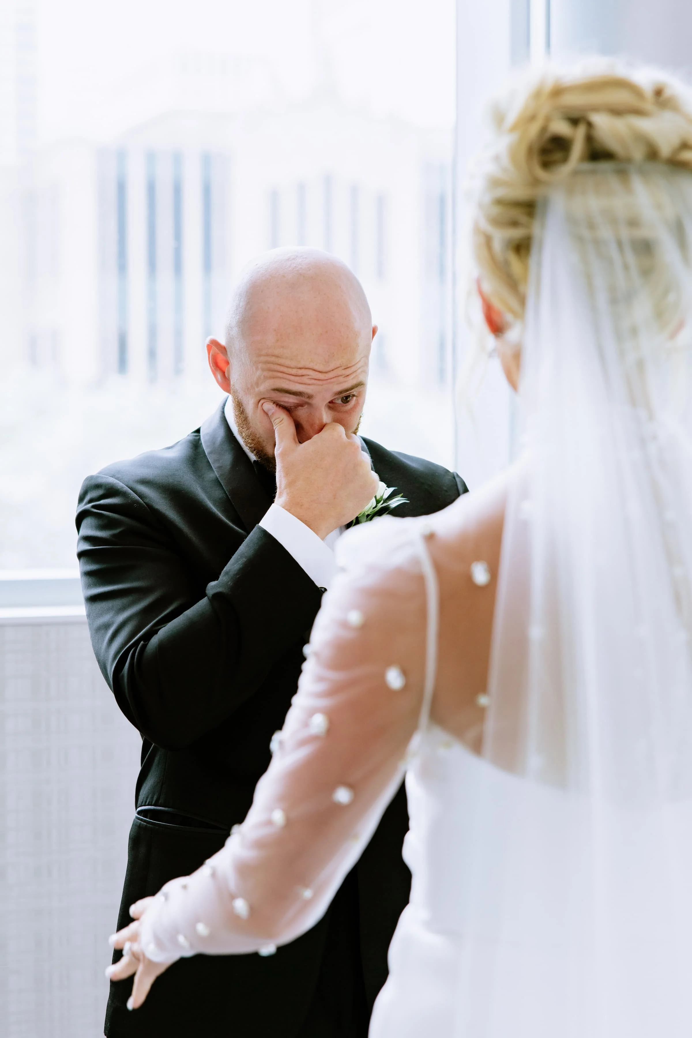A groom wiping away tears during his wedding ceremony, with a bride facing him.
