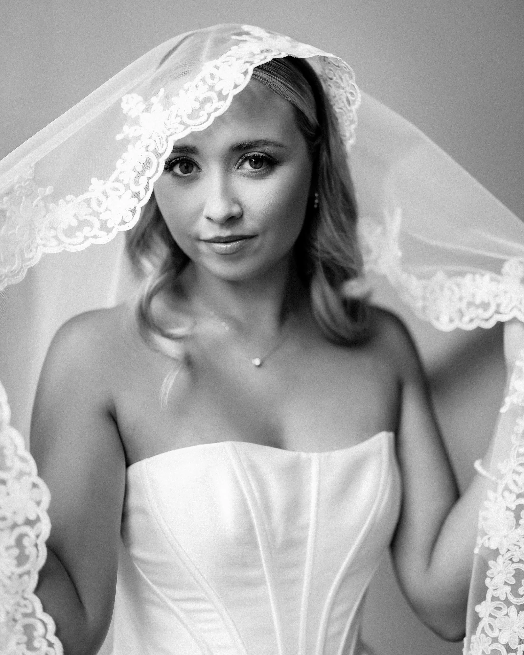 Black and white portrait of a young woman in a strapless dress with a lace veil draped over her head.