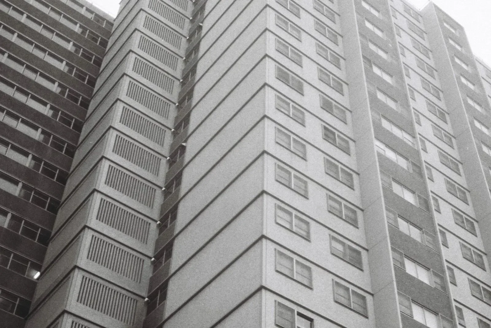 Black and white photo of a high-rise apartment building with numerous windows and balconies, viewed from below.