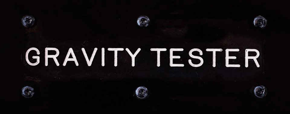 A black switch label from a control panel of the bluebird flying saucer, with the text 'GRAVITY TESTER' in white letters, fixed with screws.