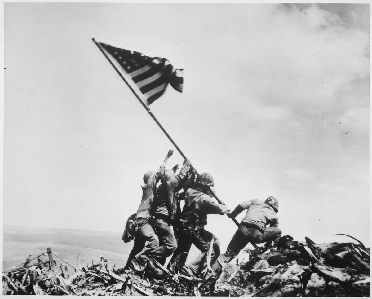 Image showing four soldiers in the process of raising tall American flab on a hill.