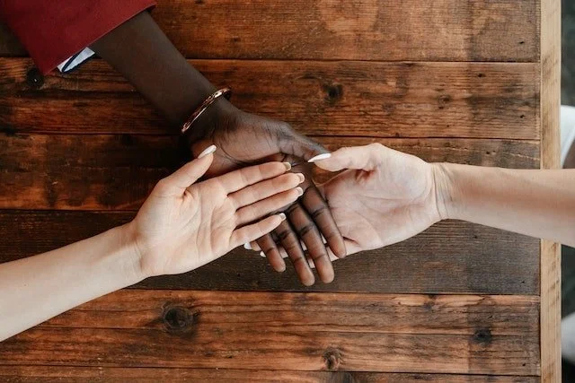 zoomed photo of three diverse hands on top of another on a wood table