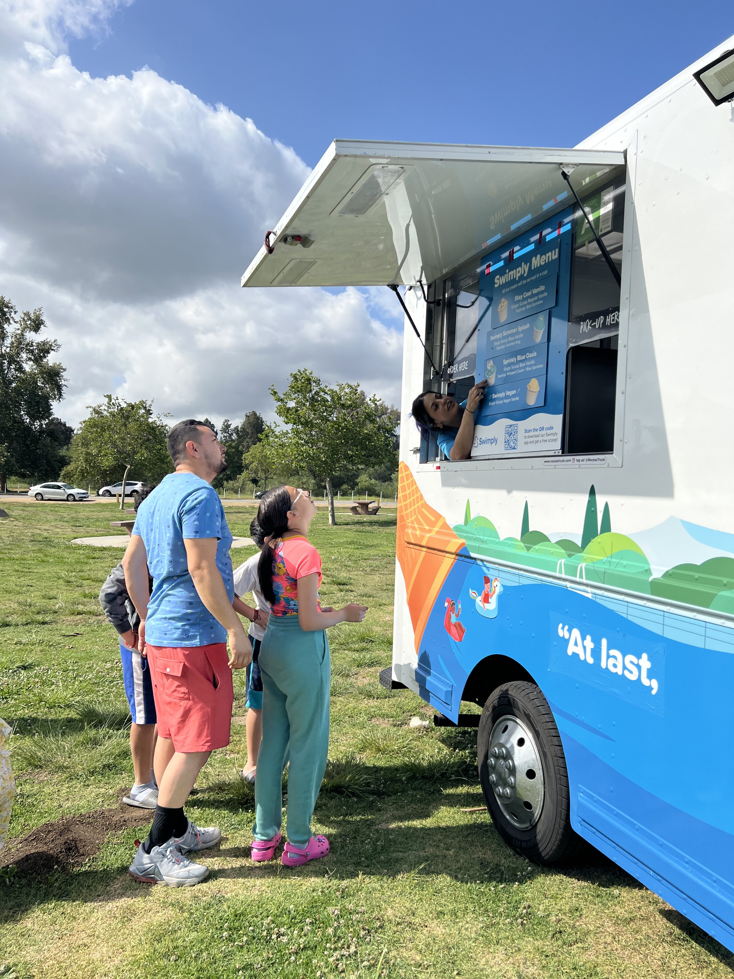 The photo shows a family waiting to be served outside of the Swimply branded truck