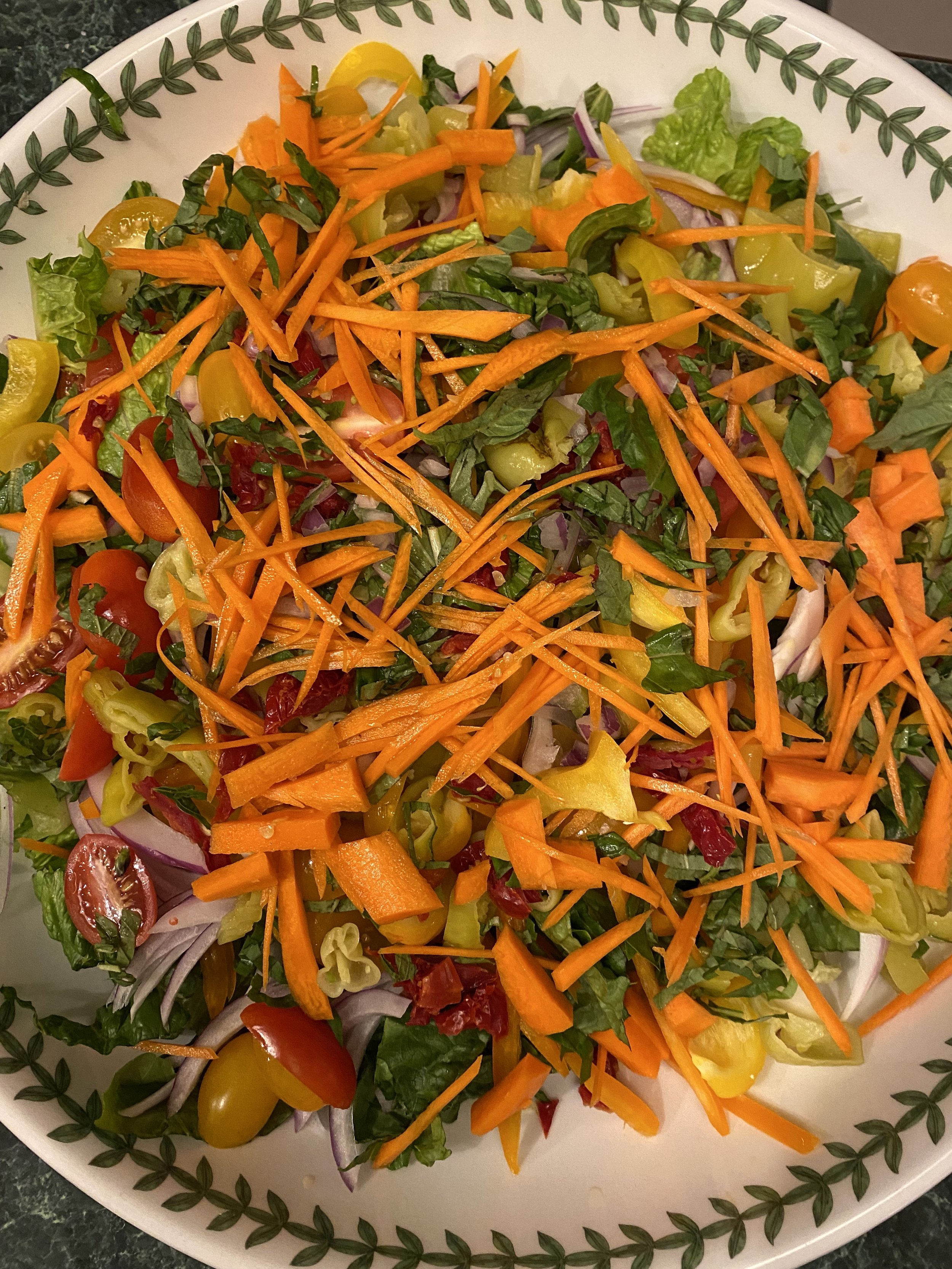 colorful salad in a white bowl with carrots, tomatoes, yellow bell peppers, pepperoncini and fresh basil