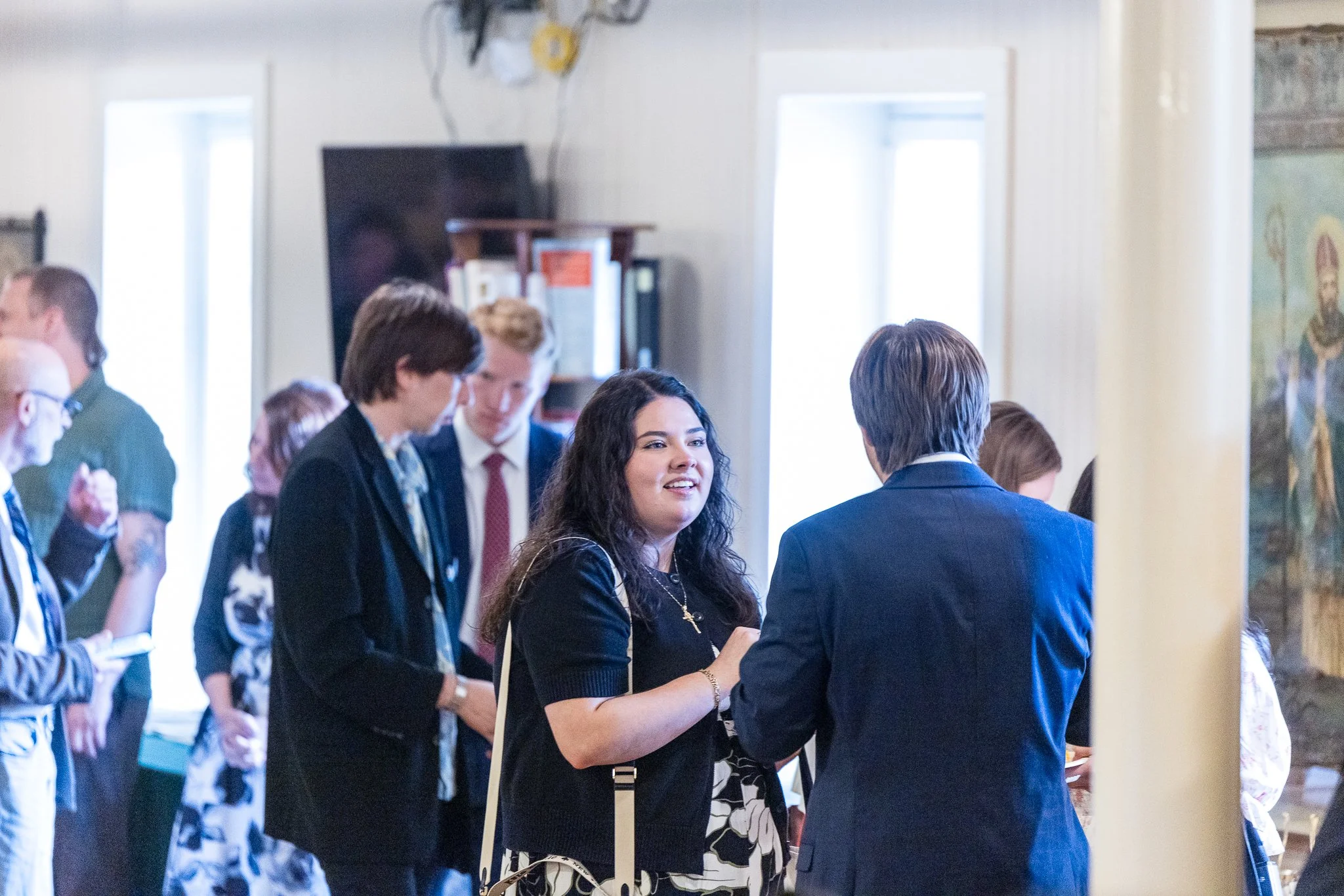 People socializing at a gathering or event in a well-lit room, engaging in conversation.