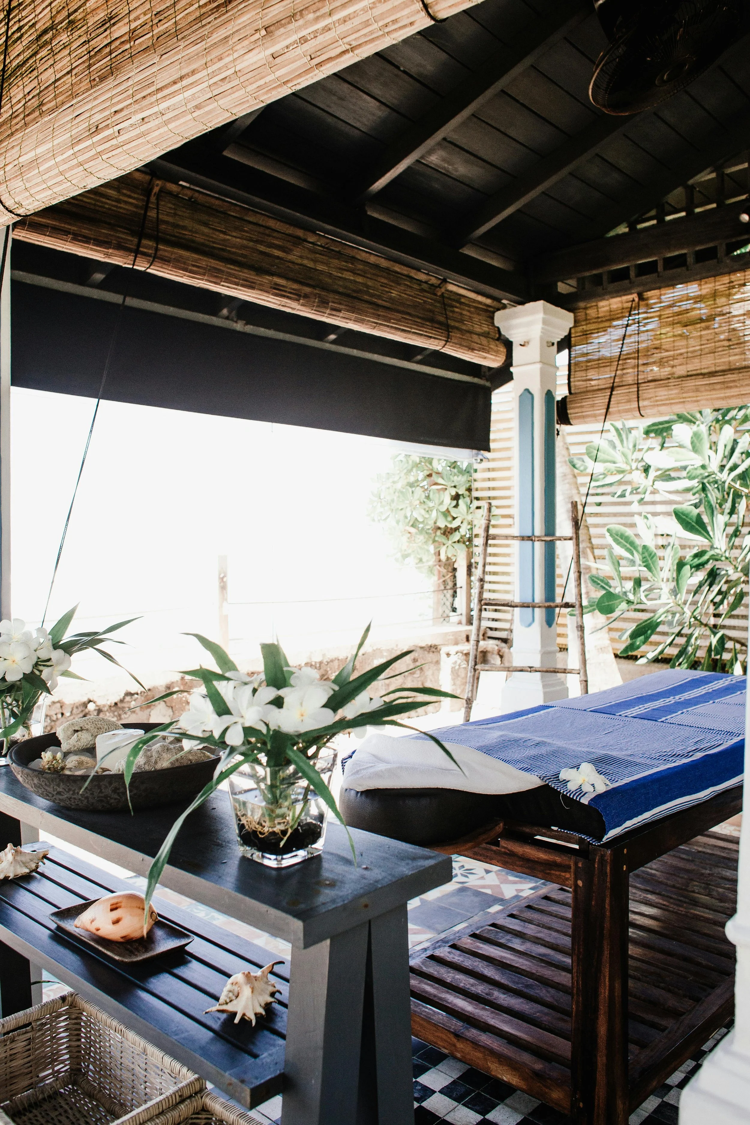 Luxury wellness treatment room with a massage table, tropical plants, and natural light, reflecting restorative bodywork, relaxation, and recovery-focused spa experiences.