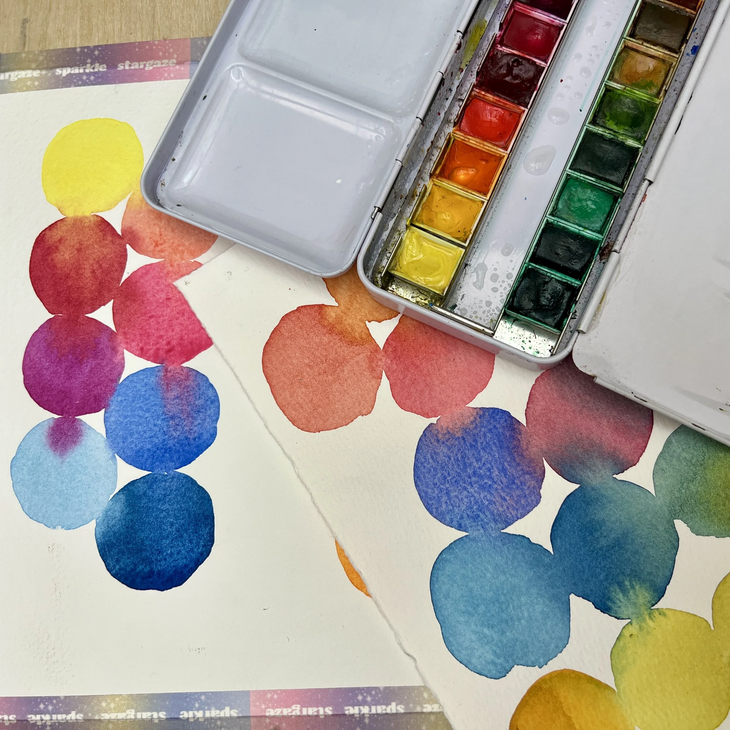 colourful paint swatches and a watercolour box on a surface
