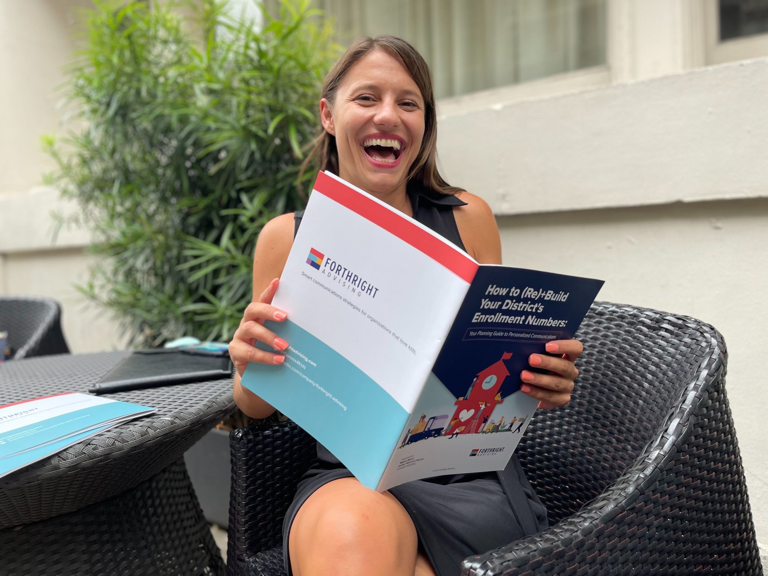  Forthright team member Niki smiles while sitting in a black dress and holding a booklet about rebuilding your district’s student enrollment numbers 