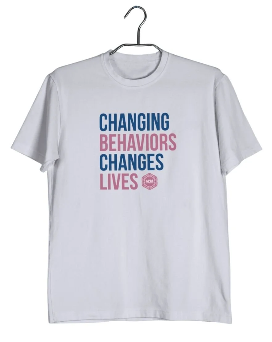 Mockup of a white t-shirt with the APBS conference logo and text reading Changing Behaviors Changes Lives in navy and pink.