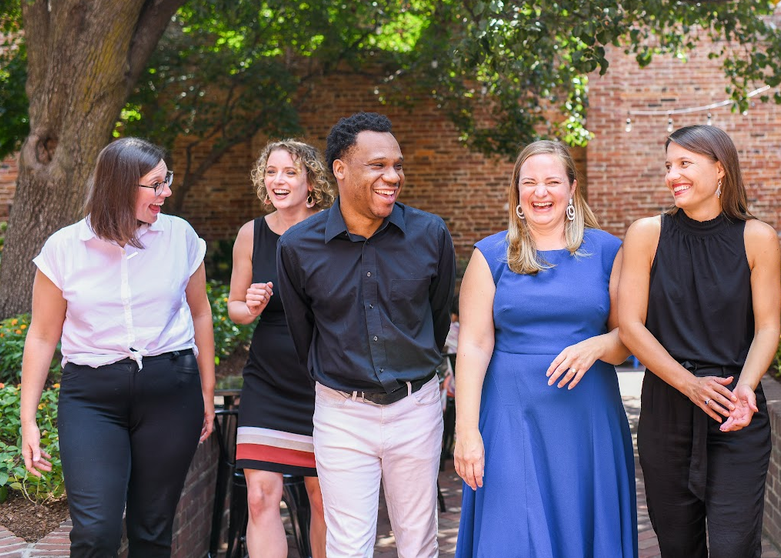 Forthright Advising team members Lauren, Ashley, Michael, Katie and Niki walking outside with a brick wall and trees in the background