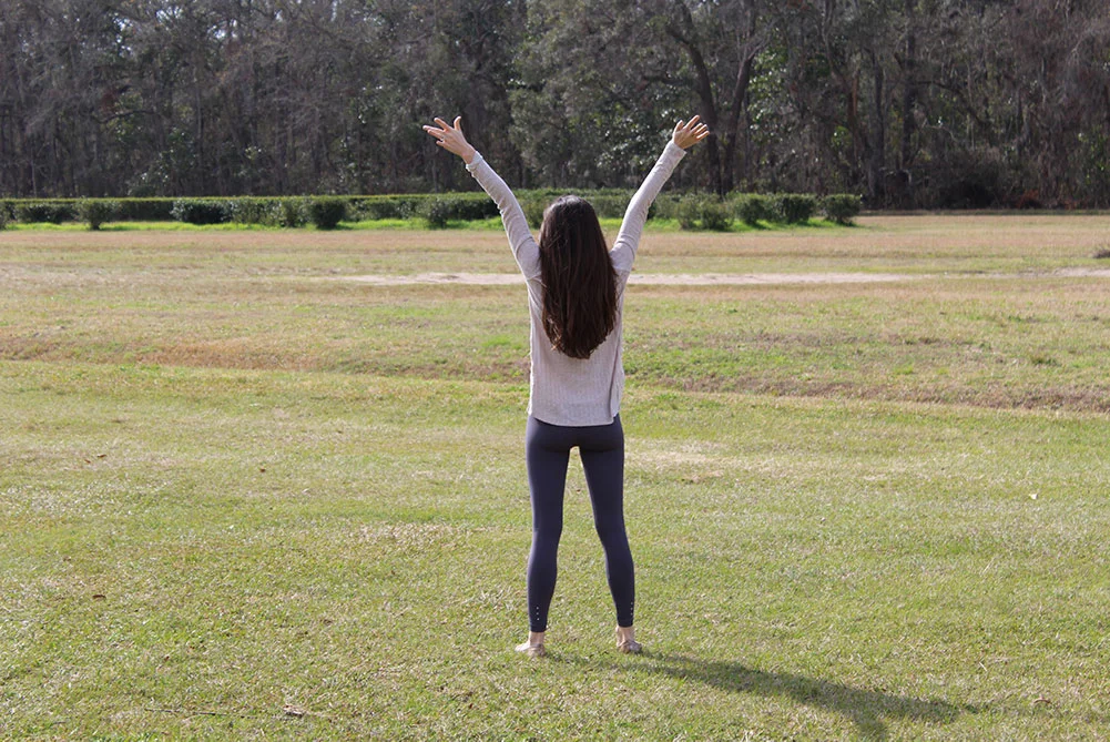 Woman standing in field with arms in the air, shown from behind