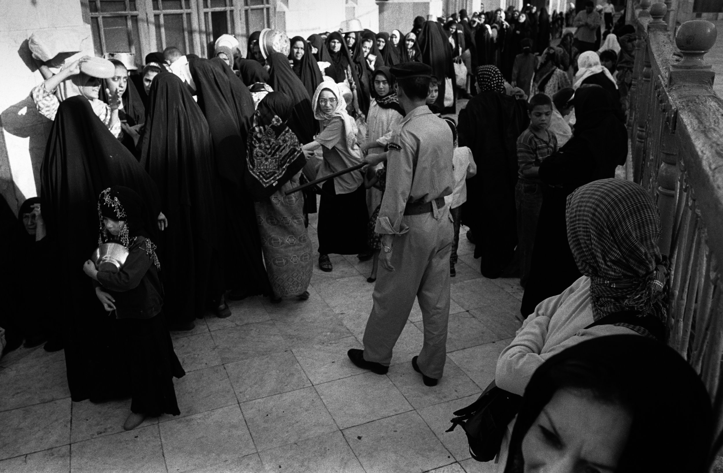  At the Al-Khazani Mosque in Baghdad, Iraq women wait for a free meal as a policeman keeps them in line. 