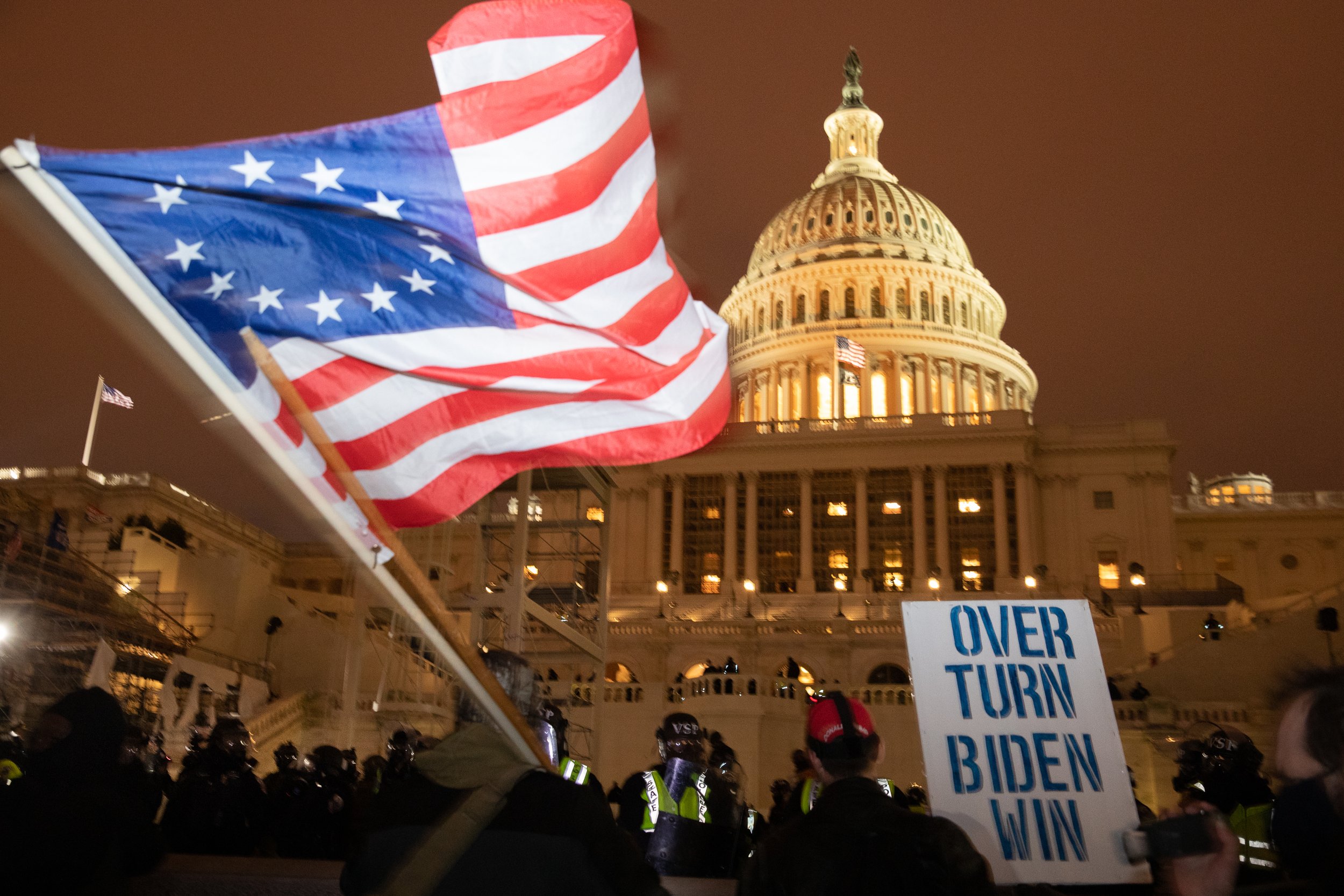  The Betsy Ross flag, sometimes used by white supremacist groups, is waved in front of the Capitol as police move in to enforce a 6:00PM curfew. Washington, D.C., 6 January 2021 