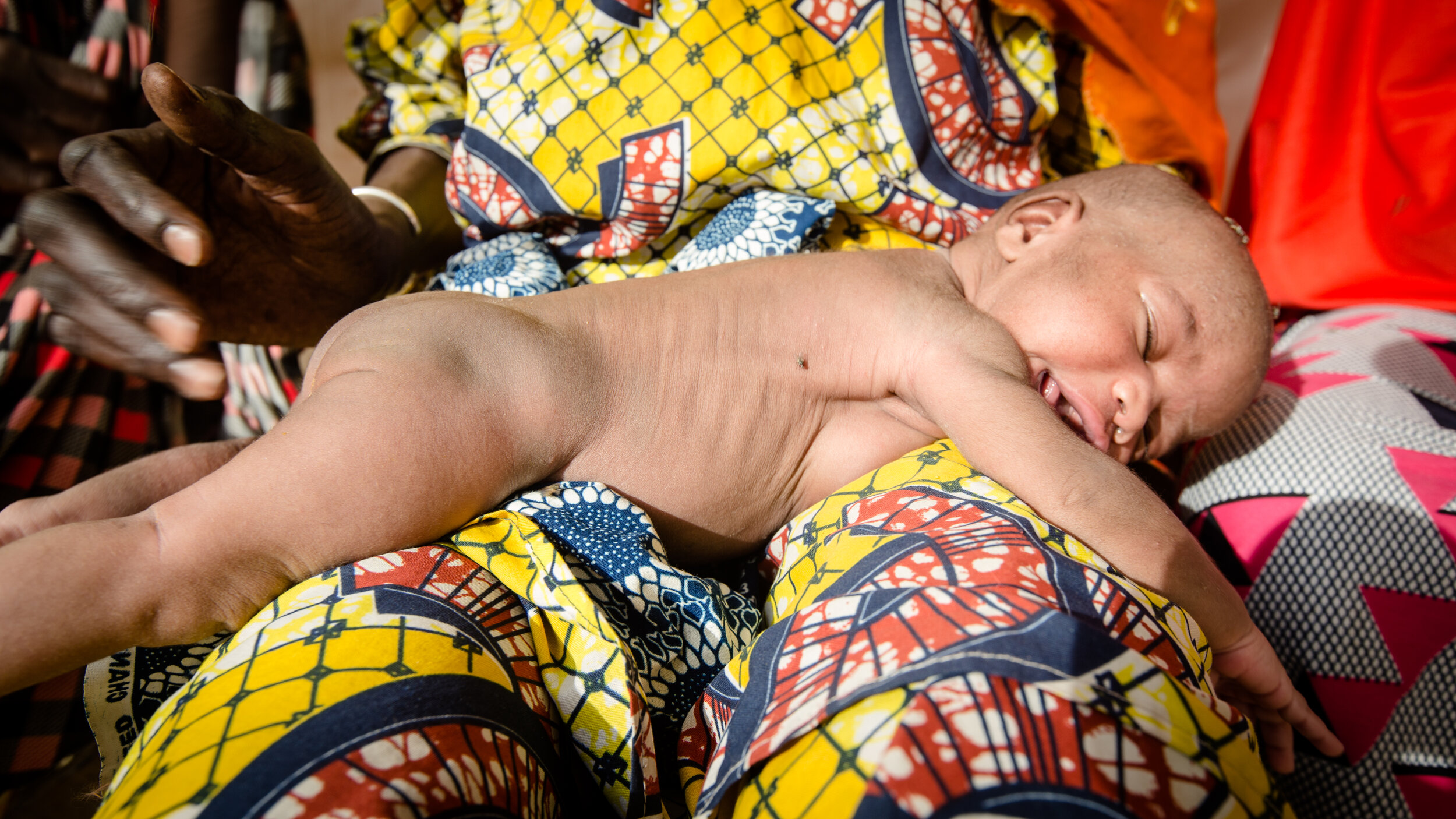  A new born sunbathing on the lap of their grandmother in front of the maternal health clinic in Monguno, Nigeria. November 2018 
