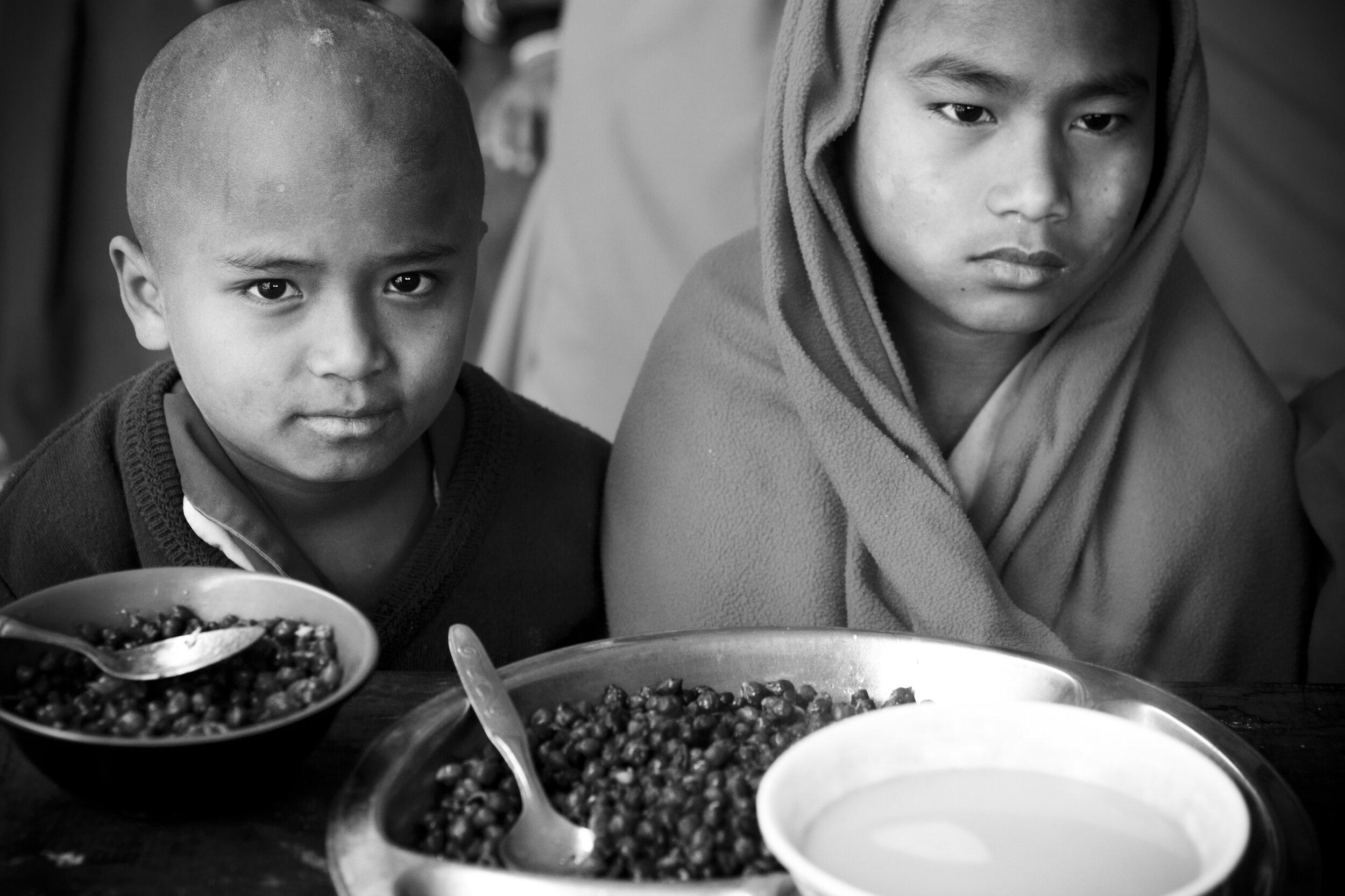  Two monks waiting for prayers to end before starting their delicious breakfast of black beans and Tibetan yak milk tea that keeps everyone warm, at Jovo Kadhampa monastery, Kathmandu, Nepal, 2014 