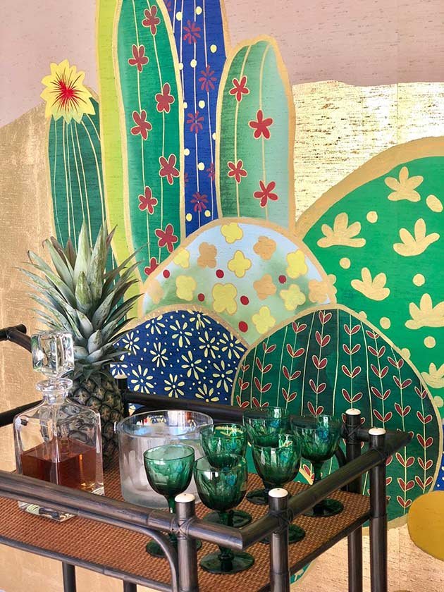  Designer bar cart setup against Joshua Desert Embellished Hand-Painted Wallpaper, featuring a cactus mural on a white wall, ideal for sophisticated interiors. 