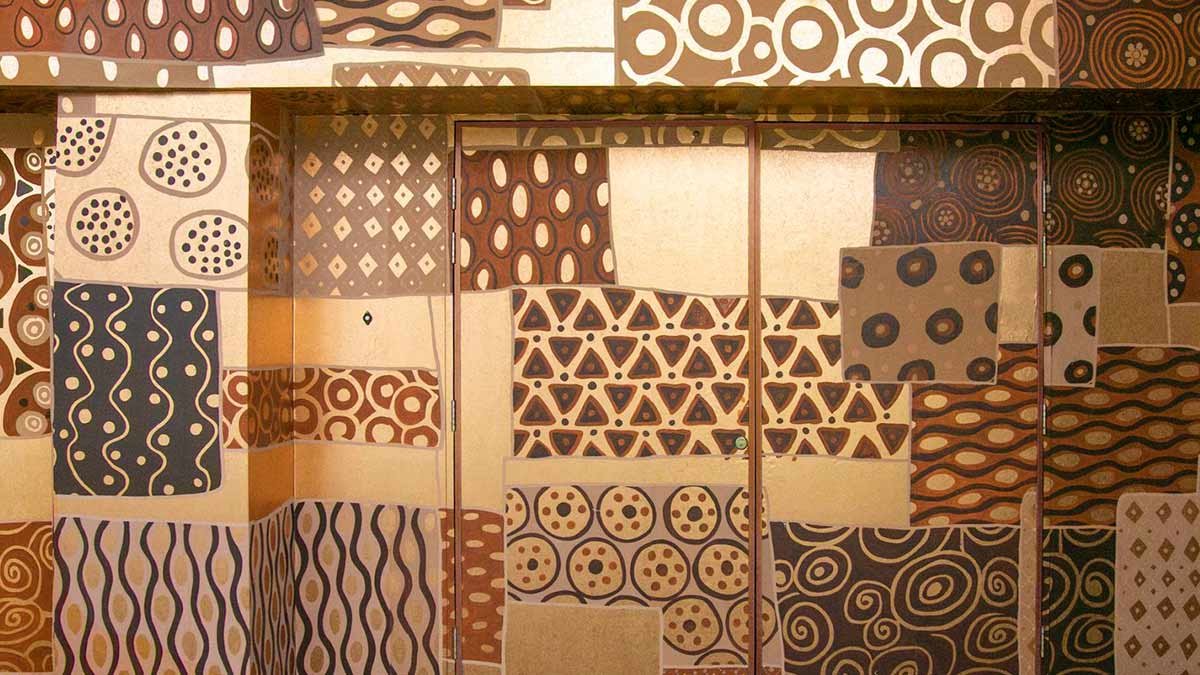  Designer Aboriginal Patchwork Wallpaper: Dynamic patterns on a light brown wooden wall, an inspiring tribute to indigenous craft, ideal for luxury oriental interior decoration. 