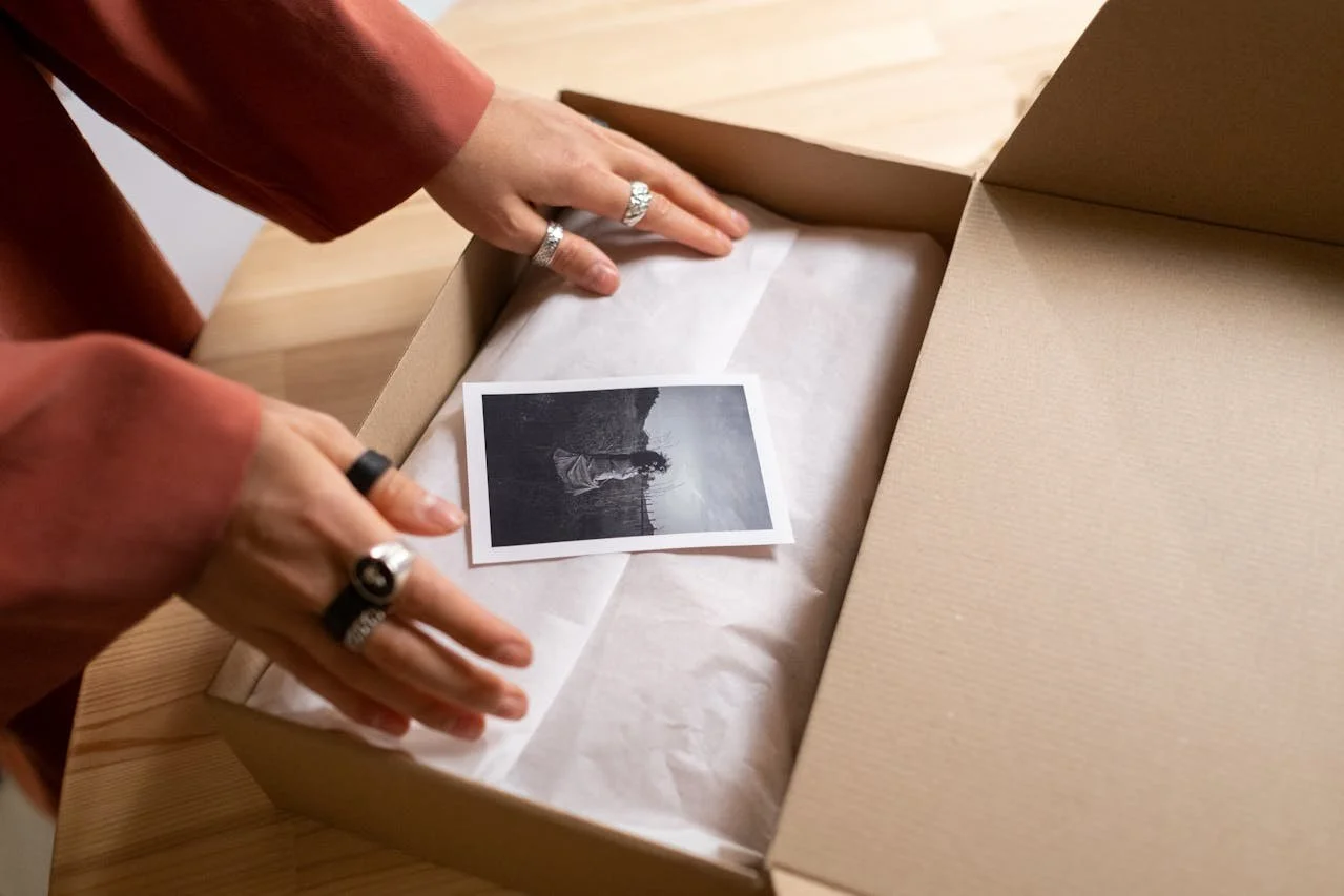 A Polaroid photo lies in a box, and two hands are reaching out for it.