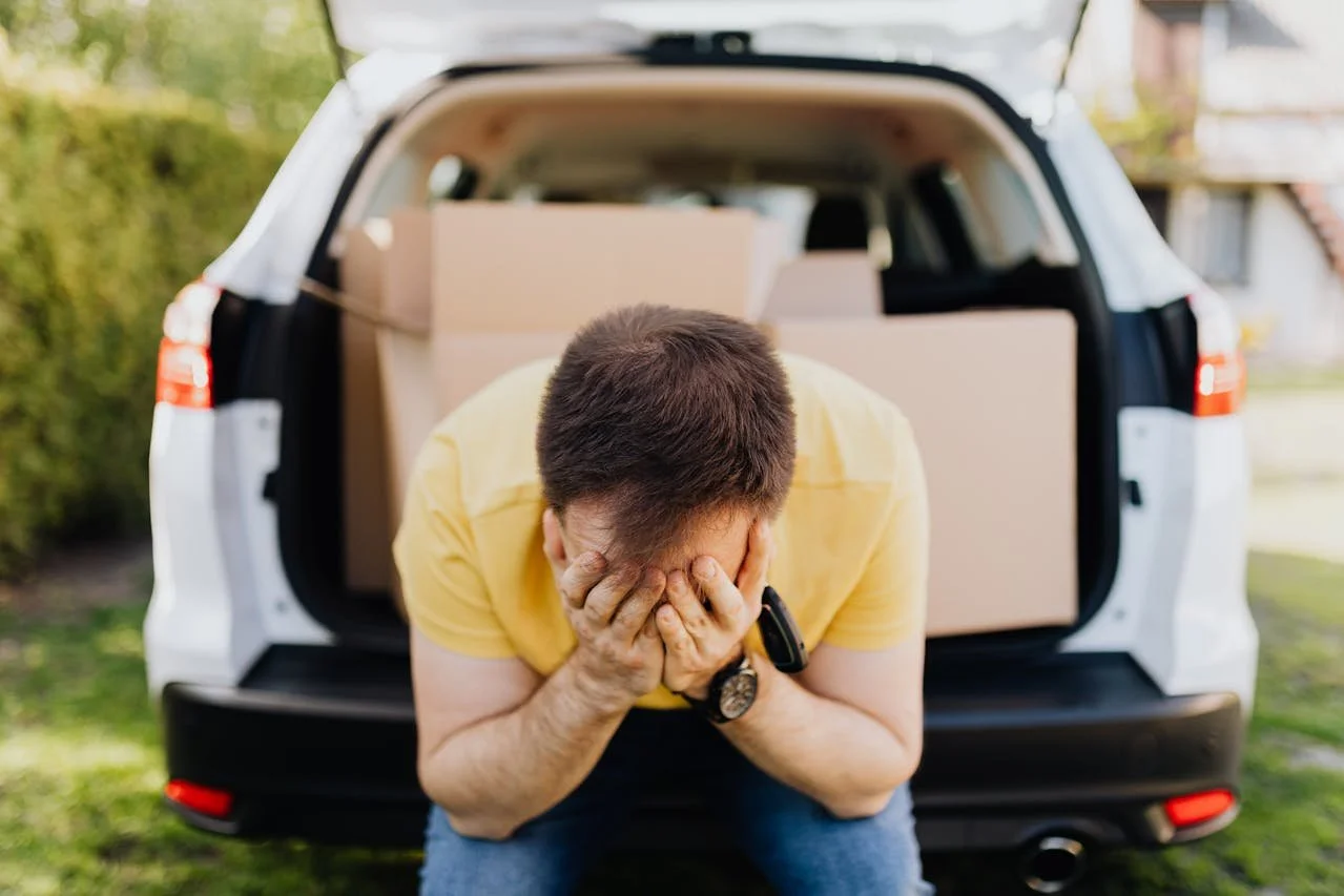 Exhausted man covering while packing his car with boxes.