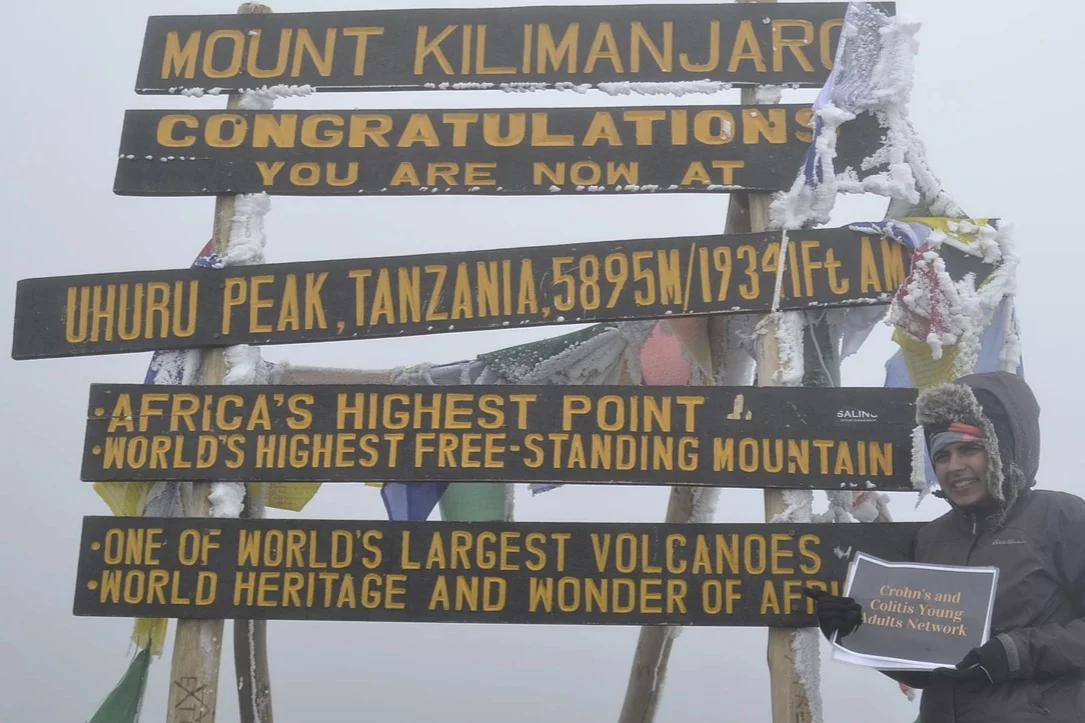 Sneha Dave at the top of Mt. Kilimanjaro. She is pictured holding a sign for the Crohn’s and Colitis Young Adult Network.