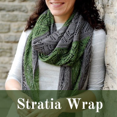 Stratia: dark grey and green lace knitted wrap is modeled by a smiling woman in a grey shirt