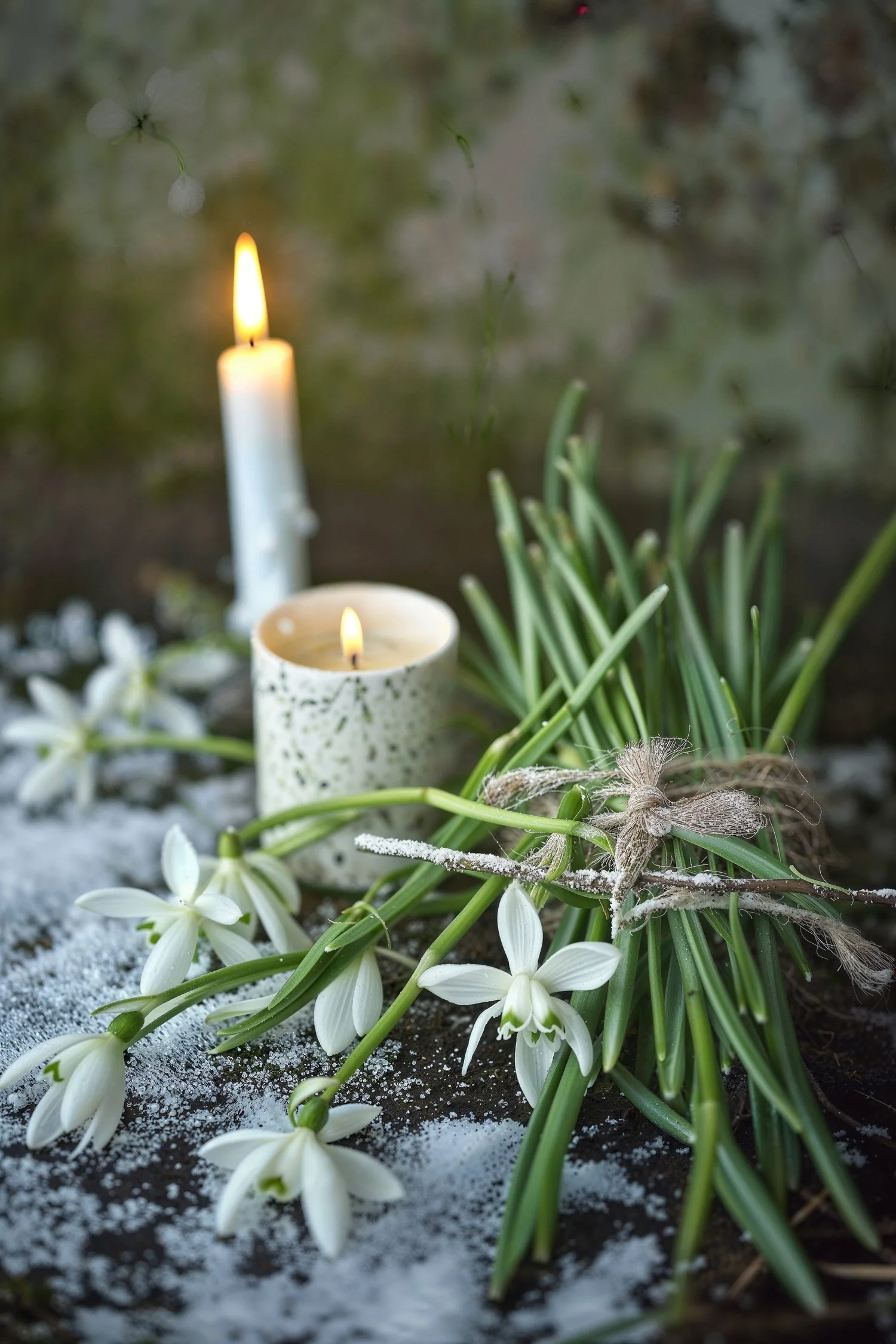 Two white candles burn near a bundle of narcissus