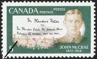 A Canadian postage stamp with a green background, an image of crosses and poppies in a field, the first two lines of In Flanders Fields, and a picture of John McCrae, with his birth and death years 1872-1918