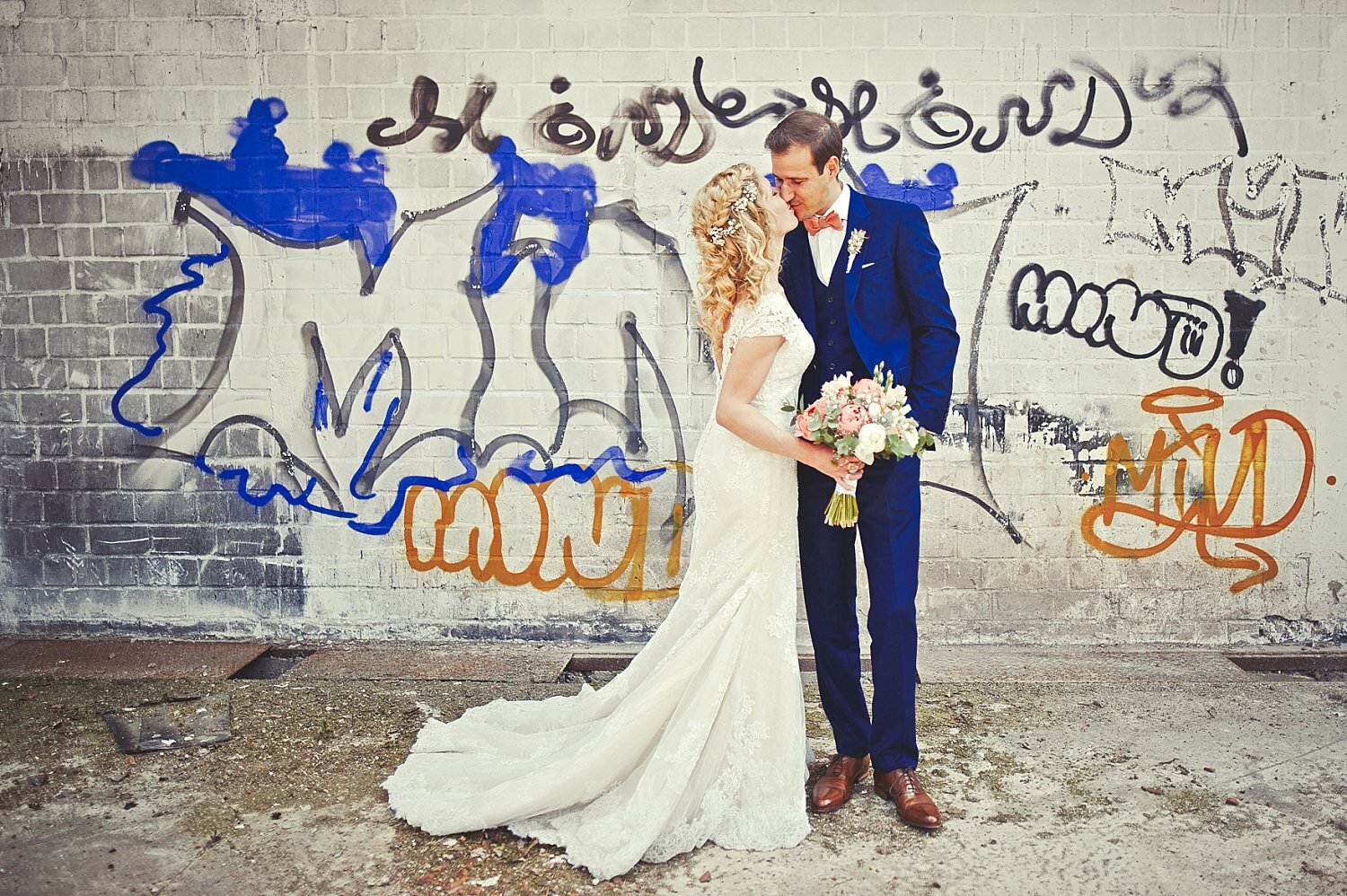 Braut und Bräutigam küssen sich vor einer Wand mit Graffiti