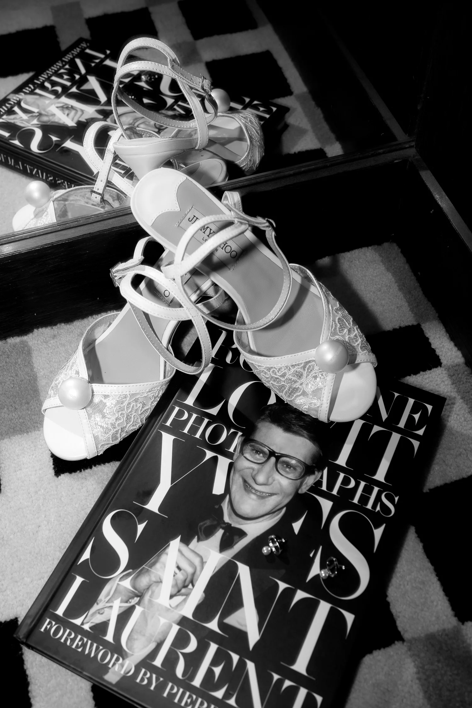 Pearl-embellished bridal shoes reflected in a mirror beside a fashion book, photographed in black and white
