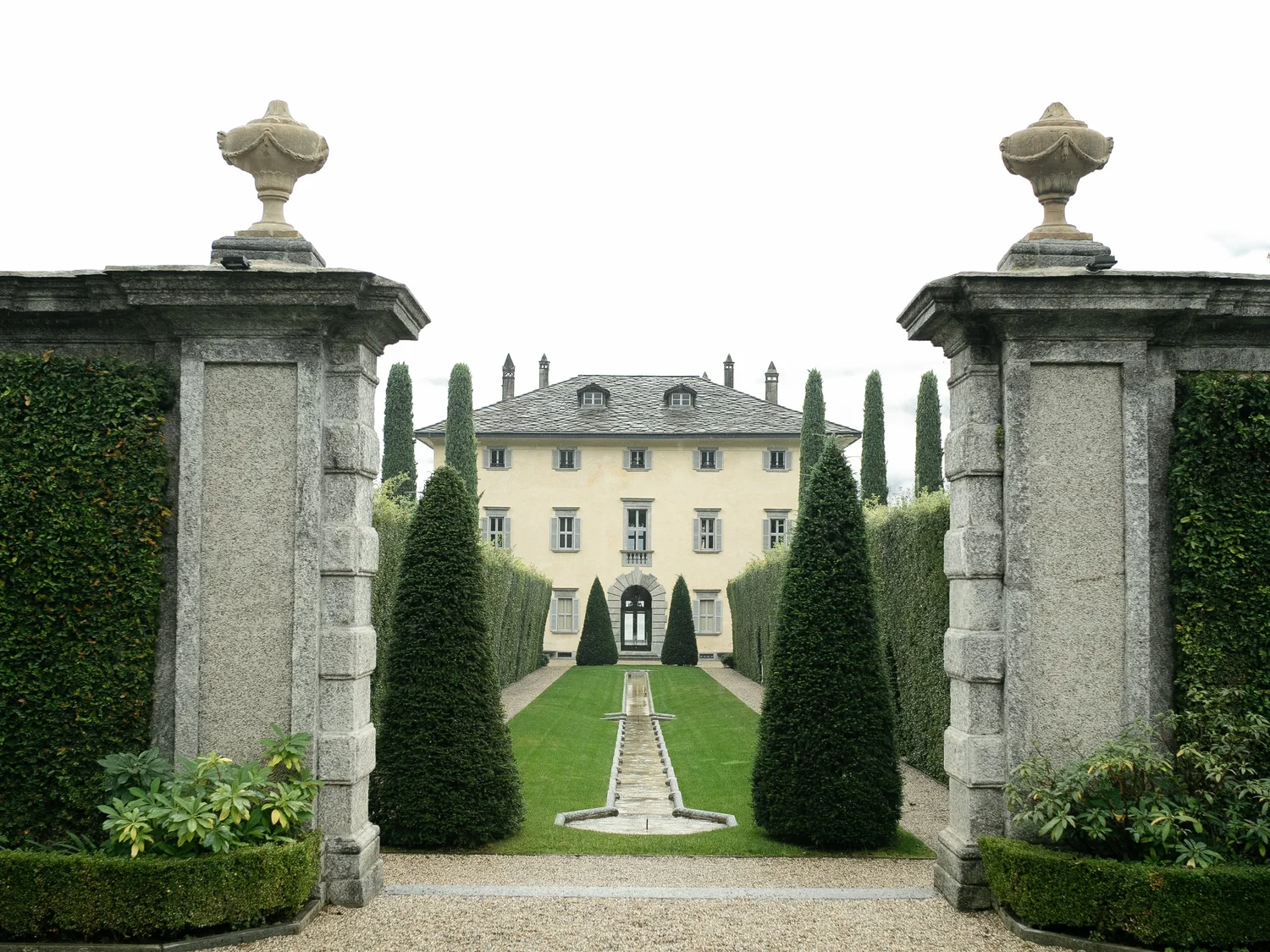 Yellow villa and formal cypress gardens framed by stone entrance gates