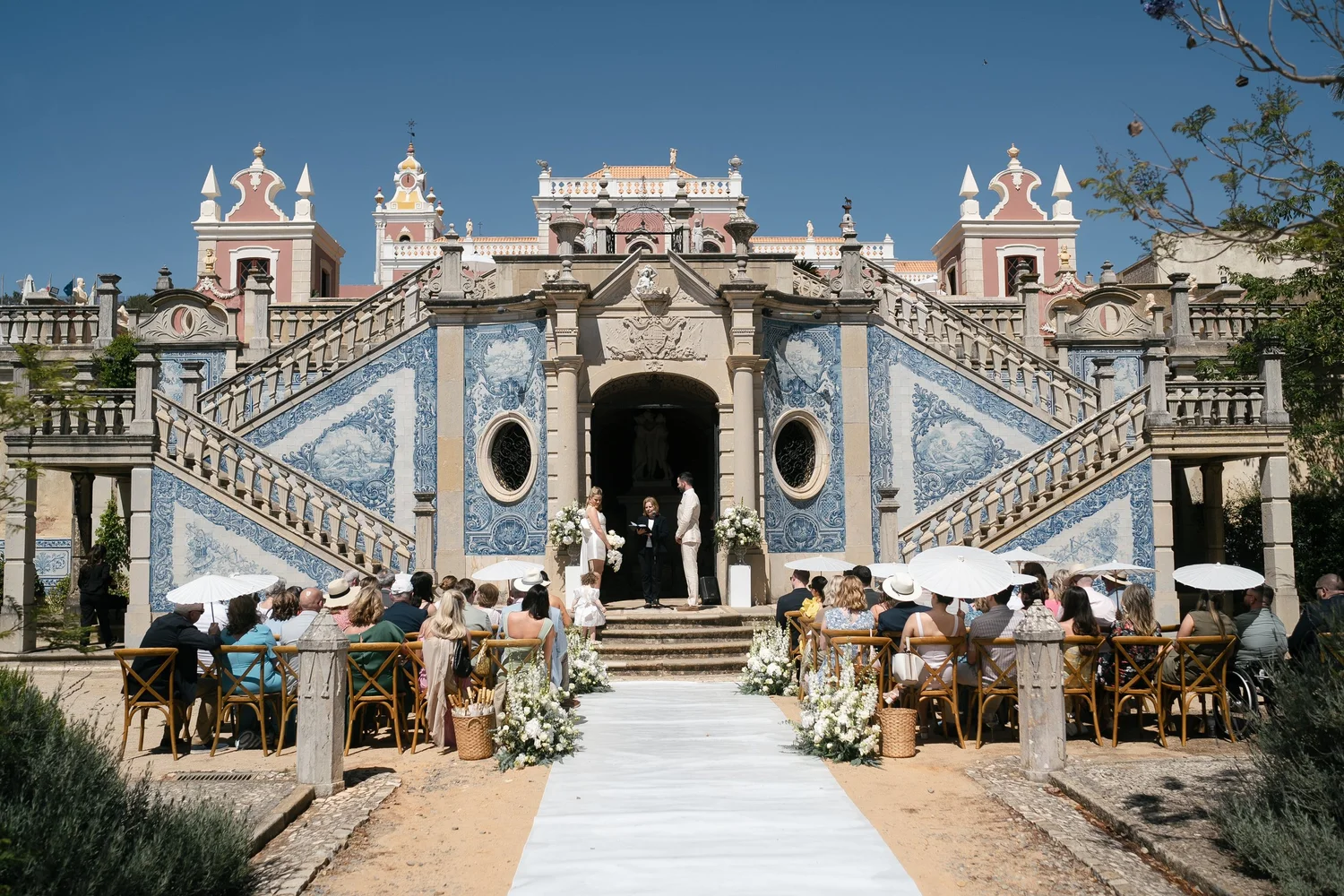 Outdoor wedding ceremony in front of ornate blue-and-white tiled stairs at a pink palace