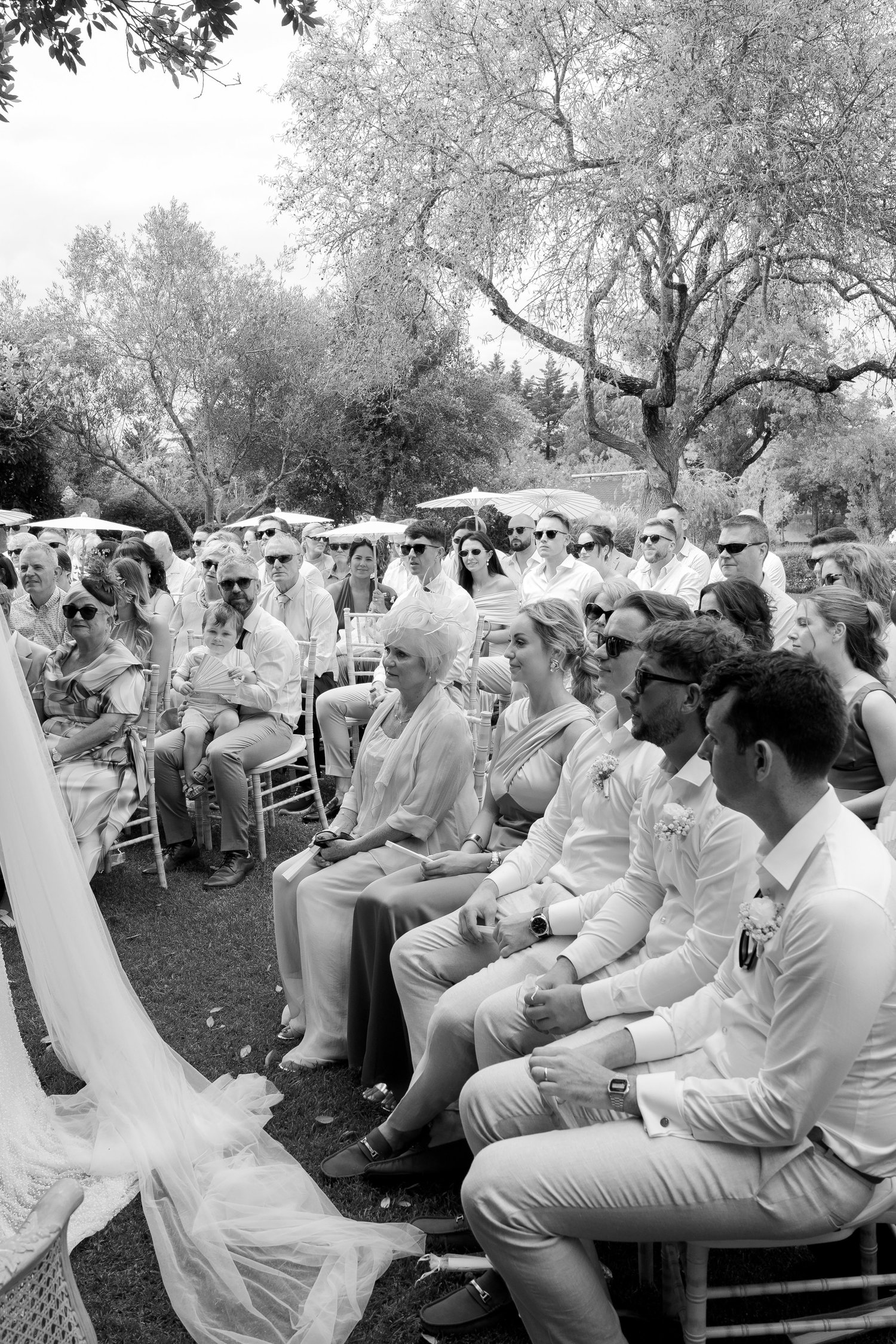 Black-and-white candid photograph of guests watching an outdoor garden wedding ceremony