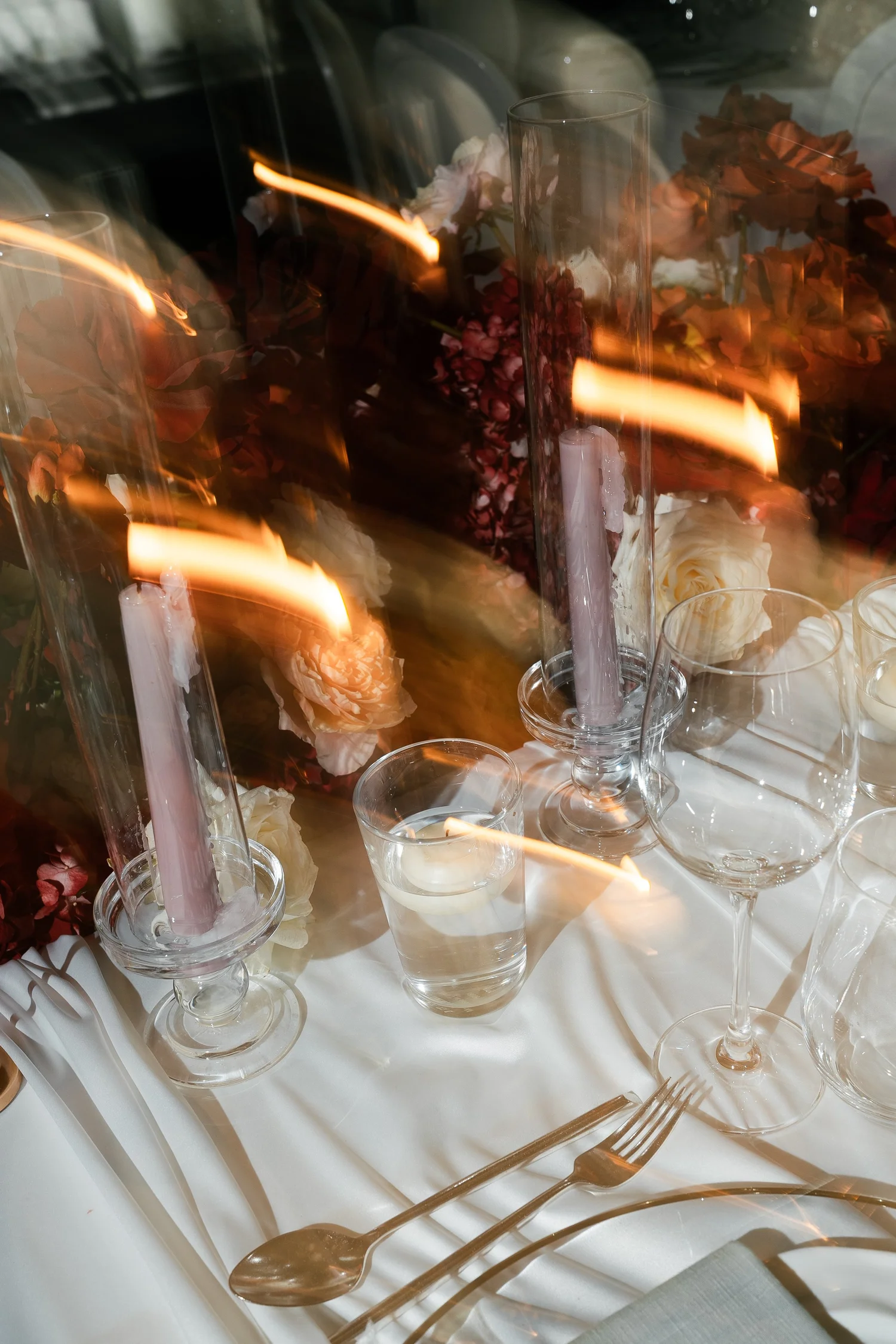 Candlelit wedding table with floral arrangements and glassware photographed with motion blur