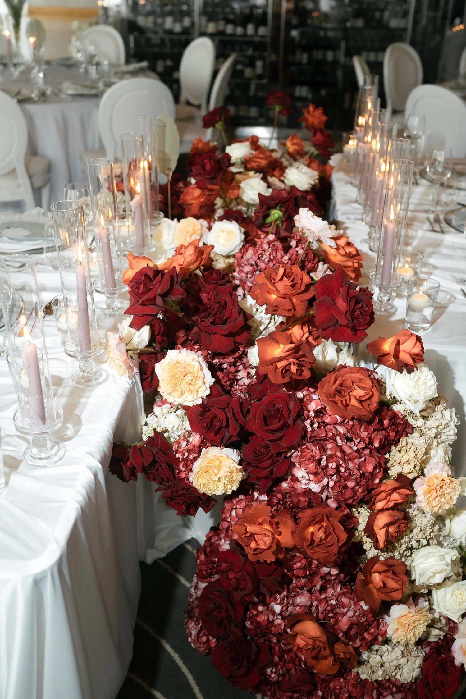 Wedding reception table with burgundy, rust and ivory flowers, glassware and candles