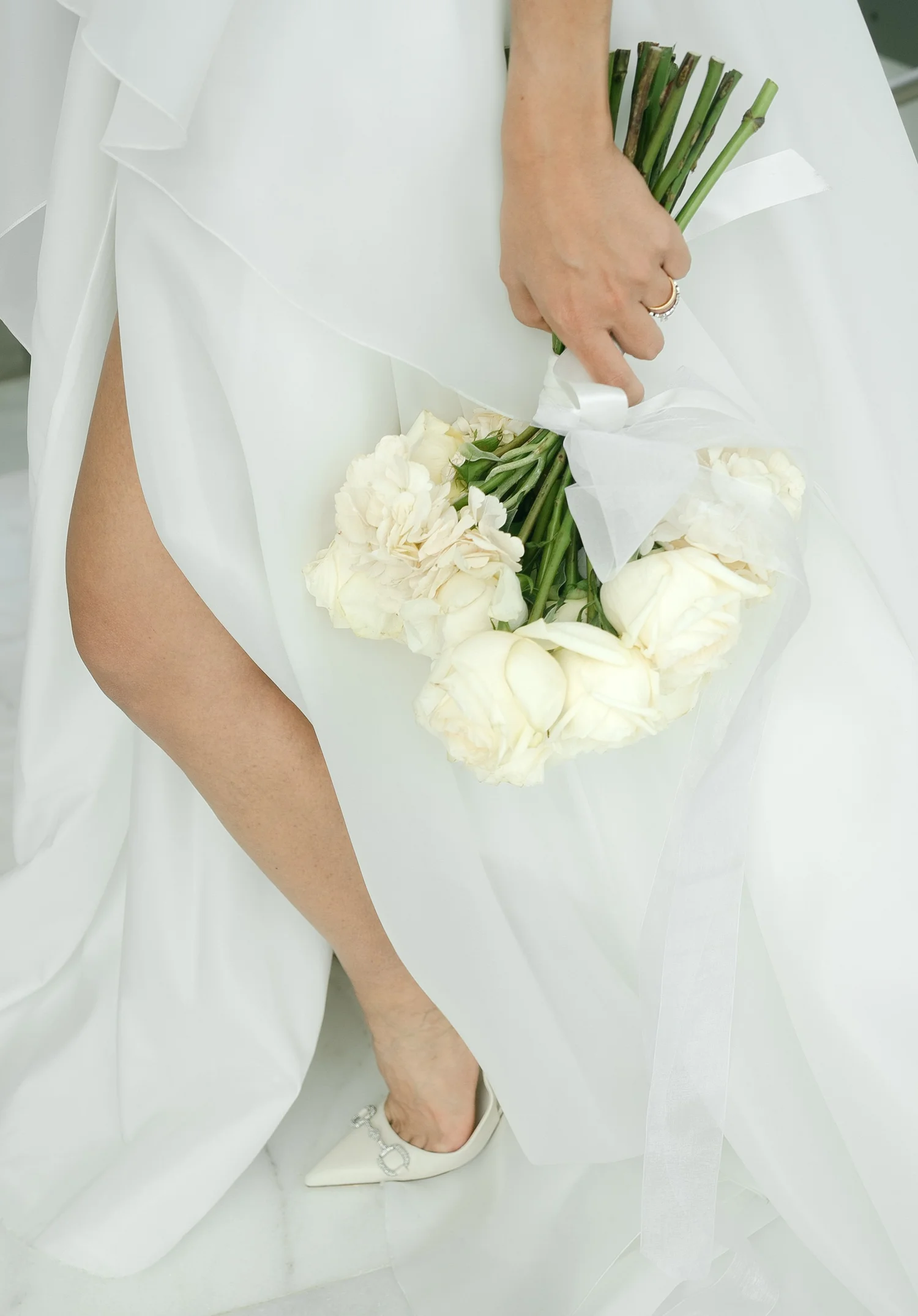 Close-up of a bride holding a white rose bouquet against her wedding gown